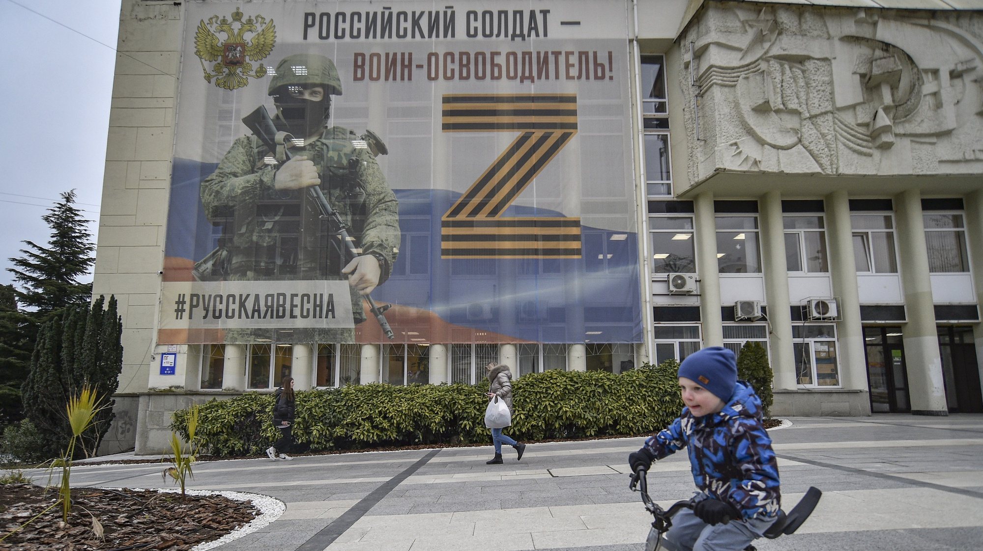 epa10524589 A child rides a bicycle in front of a building with a large banner reading &#039;Russian soldier warrior liberator. Russian spring&#039; along with the letter &#039;Z&#039; in support of Russia&#039;s armed forces involved in the country&#039;s military campaign in Ukraine, in downtown Yalta, Crimea, 15 March 2023. In February 2014 Russian forces invaded and seized control of the Crimean Peninsula. Russia declared the annexation of Crimea on 18 March 2014, two days after the celebration of a so called &#039;referendum&#039; in that territory. In a vote that reaffirmed Ukraine&#039;s &#039;national unity and territorial integrity&#039;, the United Nations General Assembly in the Resolution 68/262 condemned the referendum in Crimea stating it had &#039;no validity&#039;. After the annexation Moscow escalated its military presence on the peninsula to solidify the new status quo on the ground and since 2015, Russia approved the &#039;Day of Reunification of Crimea with Russia&#039; as a holiday marked annually on 18 March.  EPA/STRINGER