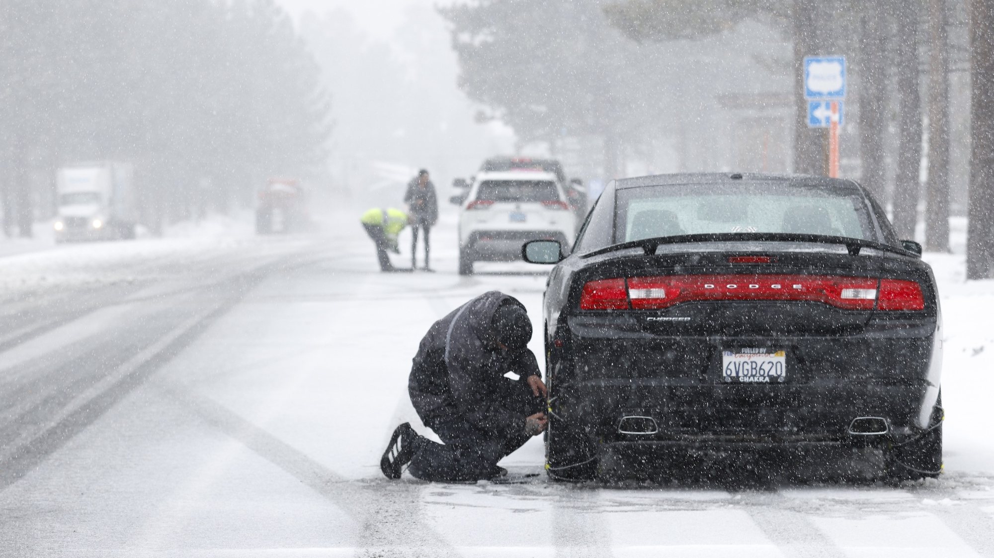 epaselect epa11192590 An individual installs a chain on the rear wheel of a car under snowfall in Mammoth Lakes, California, USA, 01 March 2024. The National Weather Service (NWS) issued a blizzard warning for Mono County until 03 March. The NWS expects winds gusting as high as 70 miles per hour in the lower elevations and above 100 miles per hour over the Sierra ridges.  EPA/CAROLINE BREHMAN
