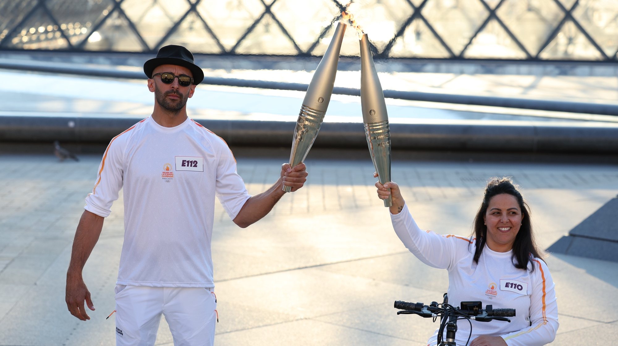 epa11478457 French artist JR (L) and Paralympic athlete Sandra Loura hold the torches as the Olympic Torch Relay arrives in Paris, France, 14 July 2024. The Olympic torch relay arrived in Paris on Bastille Day, the country&#039;s national holiday, and will visit some of the city&#039;s most famous landmarks on 14 and 15 July. In May 2024, the Olympic flame began its journey across France, including five overseas regions, visiting hundreds of towns and cities before the Olympic Games Opening Ceremony on 26 July.  EPA/JULIEN MATTIA