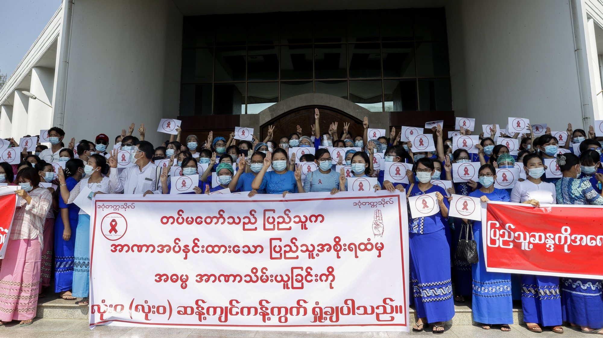 epa08988239 Teachers of Dagon University hold up placards and flash the three-finger salute as a sign of defiance during a civil disobedience campaign against the military coup, in Yangon, Myanmar, 05 February 2021. Teachers and students joined a nationwide strike as part of a civil disobedience campaign started by medical workers protesting against the recent military coup. Aung San Suu Kyi and other top political leaders were detained in a military coup on 01 February amid allegations of voter fraud in the November 2020 elections.  EPA/LYNN BO BO