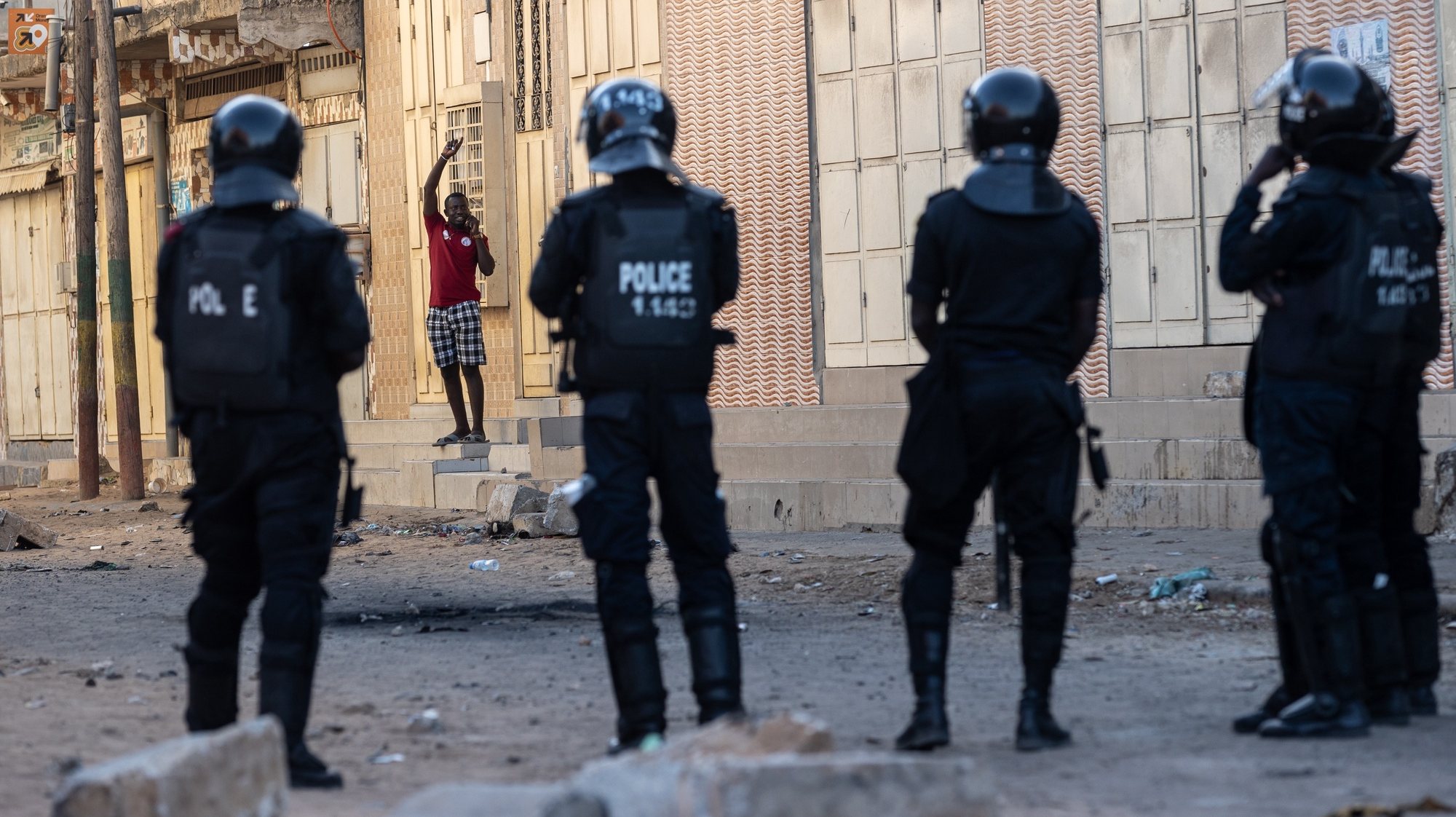 epa10671655 A local resident waves from a doorstep as police conduct an operation during a riot in Dakar, Senegal, 03 June 2023. Riots have taken place in Dakar and other cities in Senegal following the conviction on 01 June 2023 of opposition leader Ousmane Sonko on charges of corruption.  EPA/JEROME FAVRE