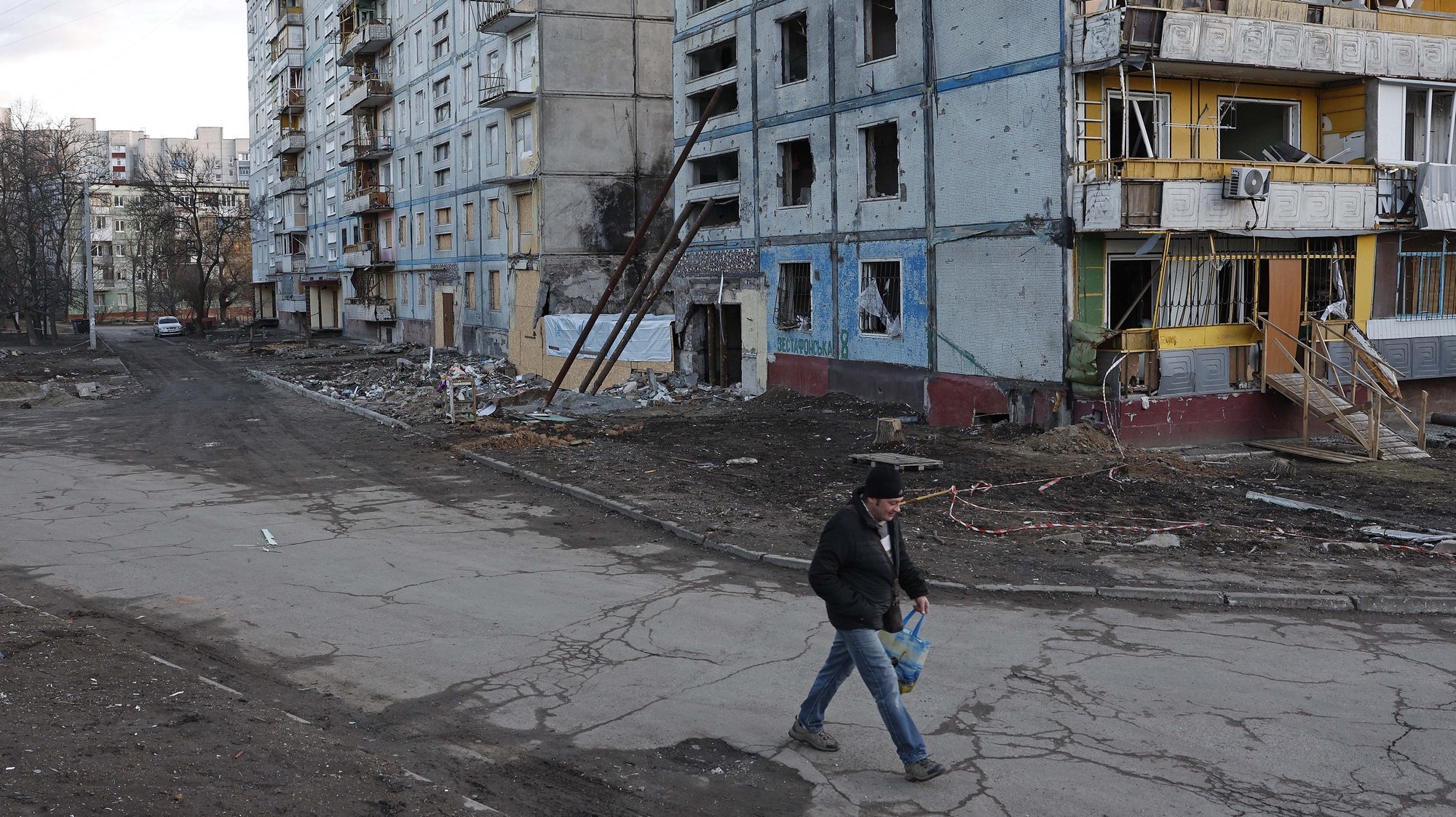 Um homem caminha junto a um bairro destruído, em Zaporizhia, 20 de fevereiro de 2023. Um ano após o início da invasão russa da Ucrânia, o balanço é composto por dezenas de milhares de mortos, milhões de refugiados e deslocados internos, cidades bombardeadas e uma economia em colapso. ANTÓNIO PEDRO SANTOS/LUSA