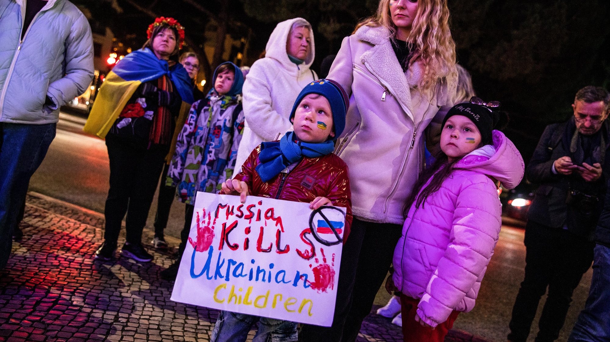 Uma crianças segura um cartaz com a frase “Russia Kills Ucraninian Children” durante uma vigília de um ano de guerra na Ucrânia, promovida pelo Núcleo da Associação dos Ucranianos em Portugal de Leiria, junto ao edifício da Câmara Municipal, 24 de fevereiro de 2023. Na ocasião é cantado o hino nacional da Ucrânia e é feito um minuto de silêncio em memória das vítimas. PAULO CUNHA/LUSA