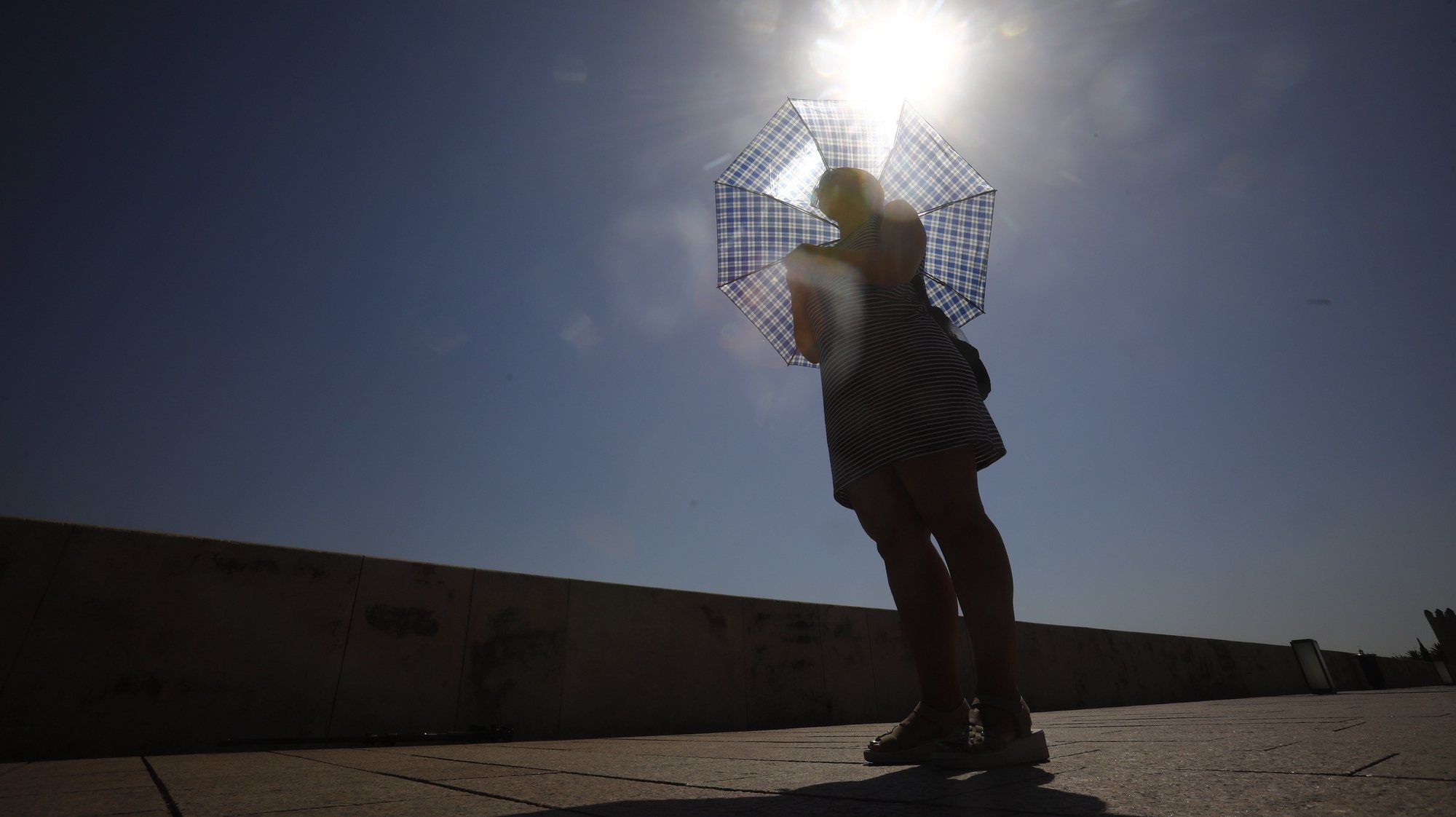 epa10101361 A woman protects herself from the sun with an umbrella as she walks across the Roman bridge in Cordoba, Spain, 01 August, 2022. The third heat wave of this summer has already begun in some areas of Andalusia and in some towns the temperatures exceeded 42 degrees on July 31.  EPA/SALAS