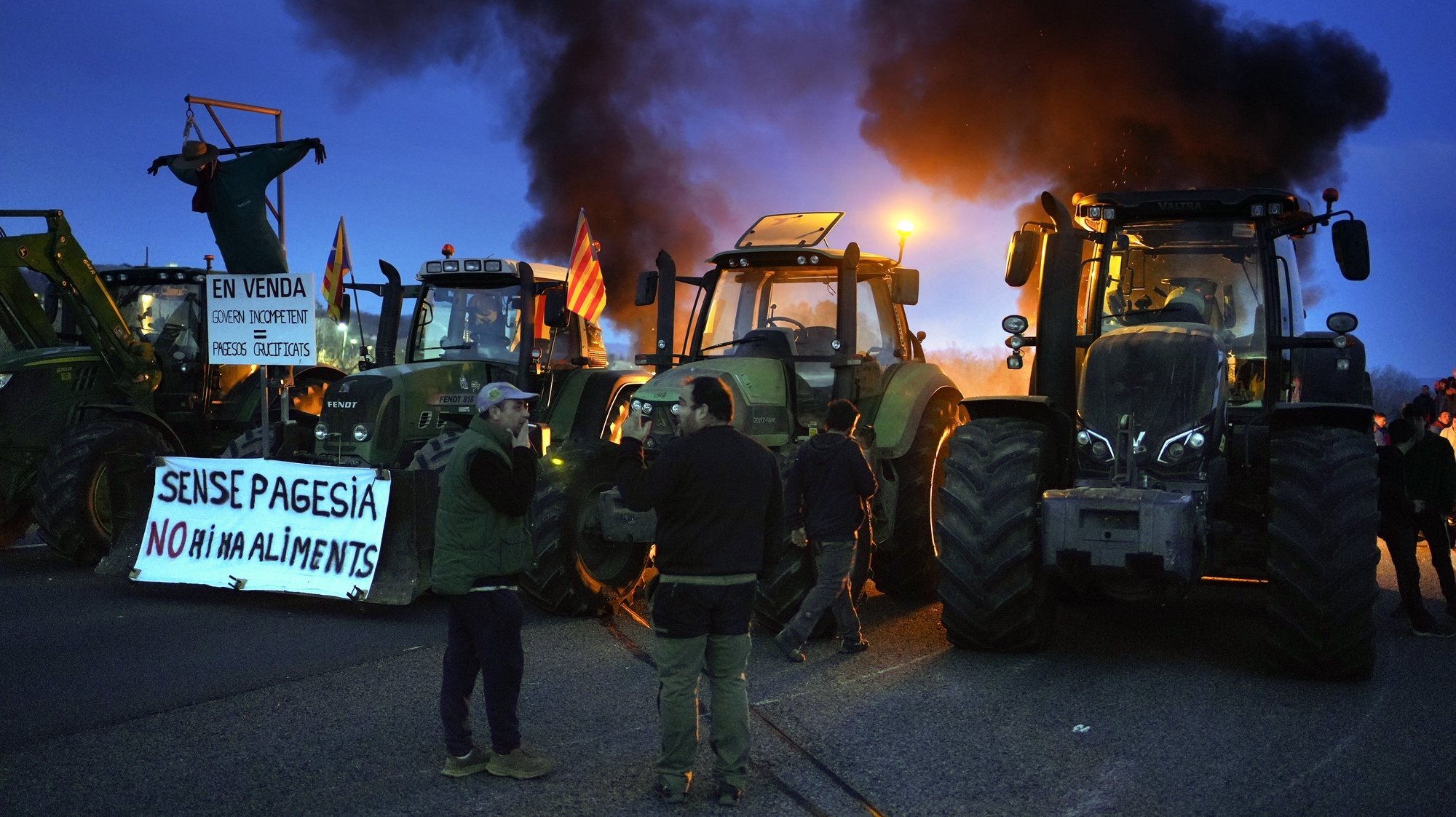 epa11132048 Farmers with their tractors blocking the AP-7 and N-II motorways light fires during a protest in Girona, Spain, 06 February 2024. Farmers in Spain continue to protest against what they say are harmful European agricultural policies, echoing demonstrations in other parts of Europe, including Germany, Belgium and France. The large sign reads &#039;no food without food&#039;.  EPA/DAVID BORRAT