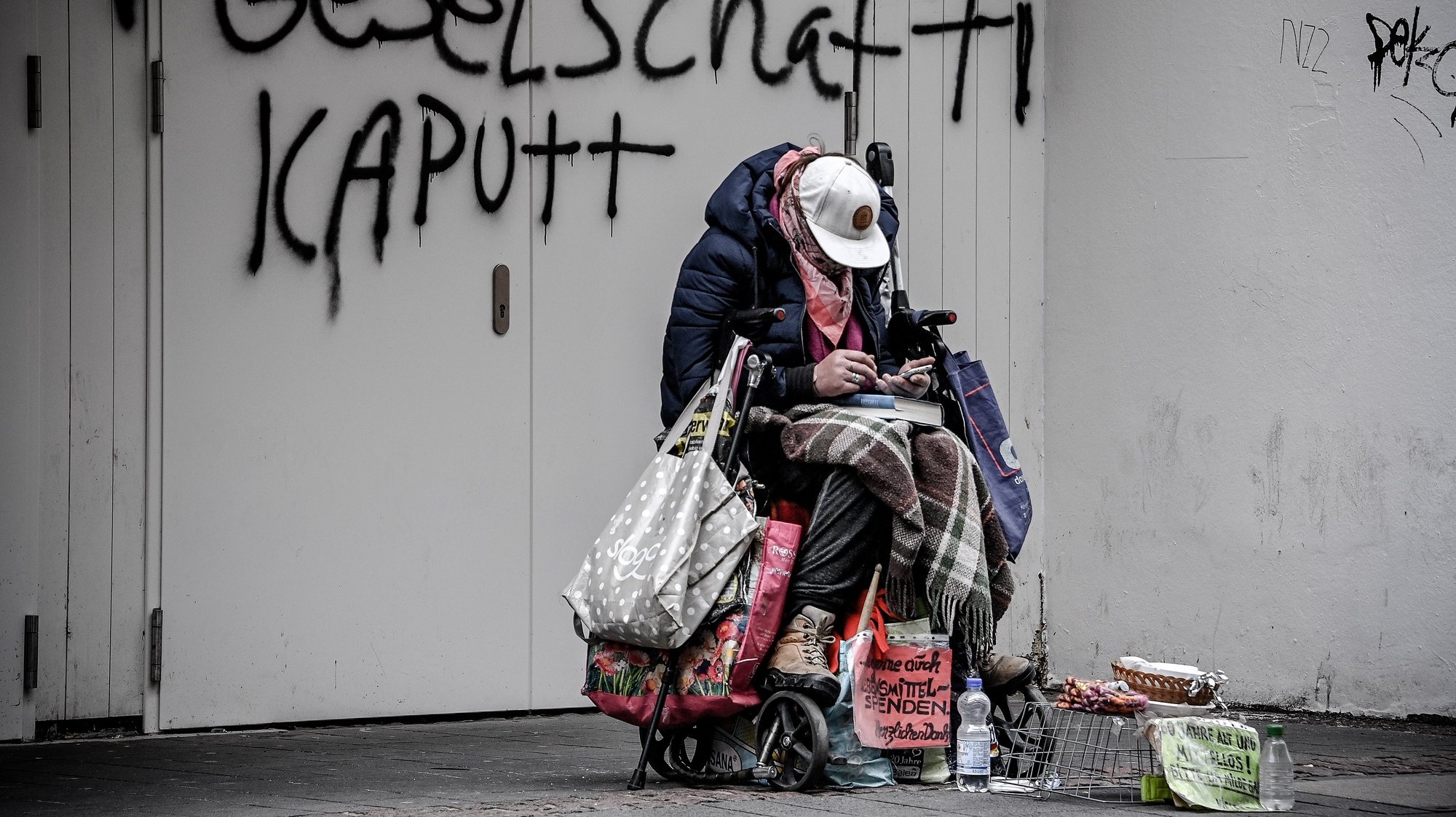 epaselect epa09069914 A homeless person sits huddled in front of a wall on which the words &#039;broken society&#039; are spray-painted, in Bonn, Germany, 12 March 2021. In Germany, many stores that had been closed for months are opening again. Shopping in stores is possible again, but must be well planned. Anyone who wants to look for clothes, shoes, electrical goods or furniture again on site must book a time slot in advance. How long that is varies by store. The shopping time must be firmly limited according to the German Corona Protection Ordinance.  EPA/SASCHA STEINBACH
