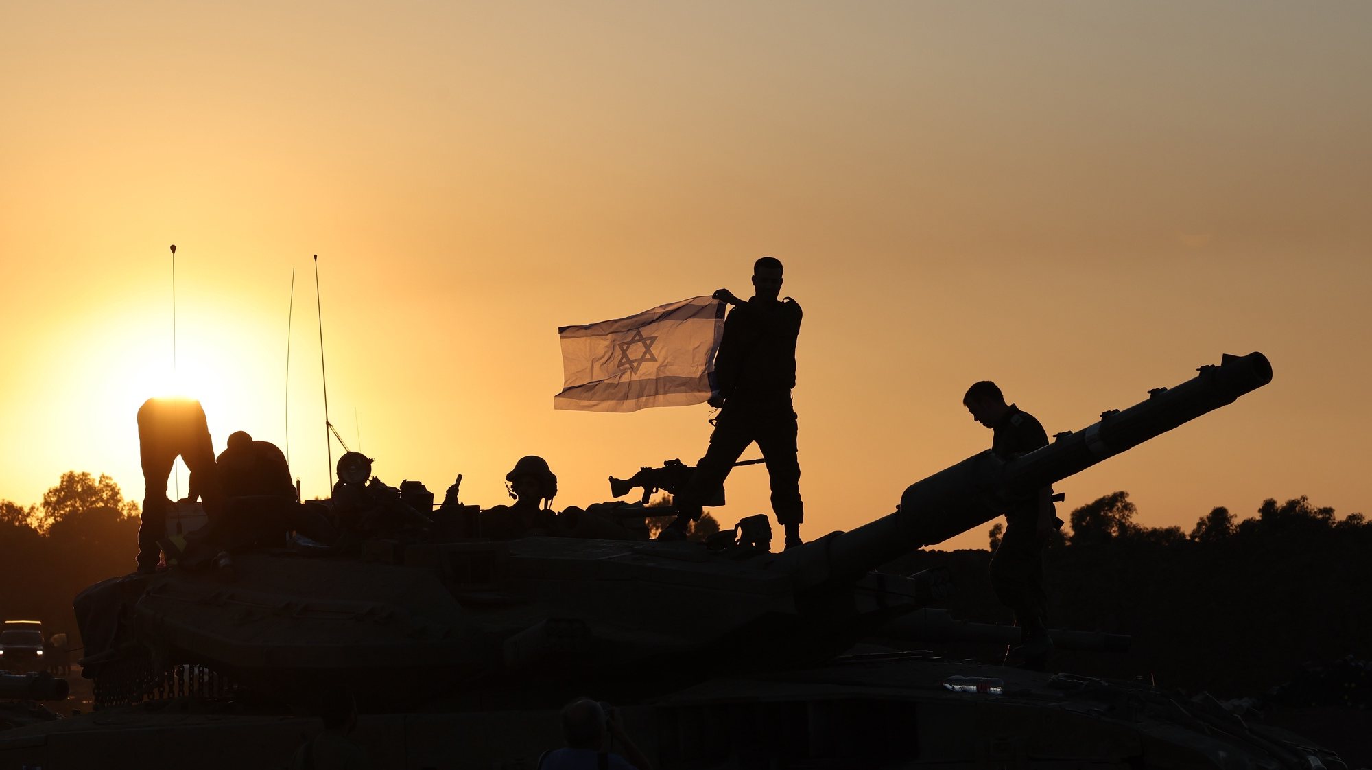 epa11001466 An Israeli soldier holds an Israeli flag while standing on top of a tank during a temporary ceasefire, near the Gaza border, in southern Israel, 29 November 2023. A four-day ceasefire agreed by Israel and Hamas was extended by 48 hours on 27 November, as more talks on a possible extension were ongoing. The Israeli army on 29 November reissued its daily message to the residents of Gaza to avoid moving back into northern Gaza which is considered a &#039;war zone&#039;, to not approach within one kilometer of the border and to not access the sea. Thousands of Israelis and Palestinians have died since the militant group Hamas launched an unprecedented attack on Israel from the Gaza Strip on 07 October, and the Israeli strikes on the Palestinian enclave which followed it.  EPA/ABIR SULTAN