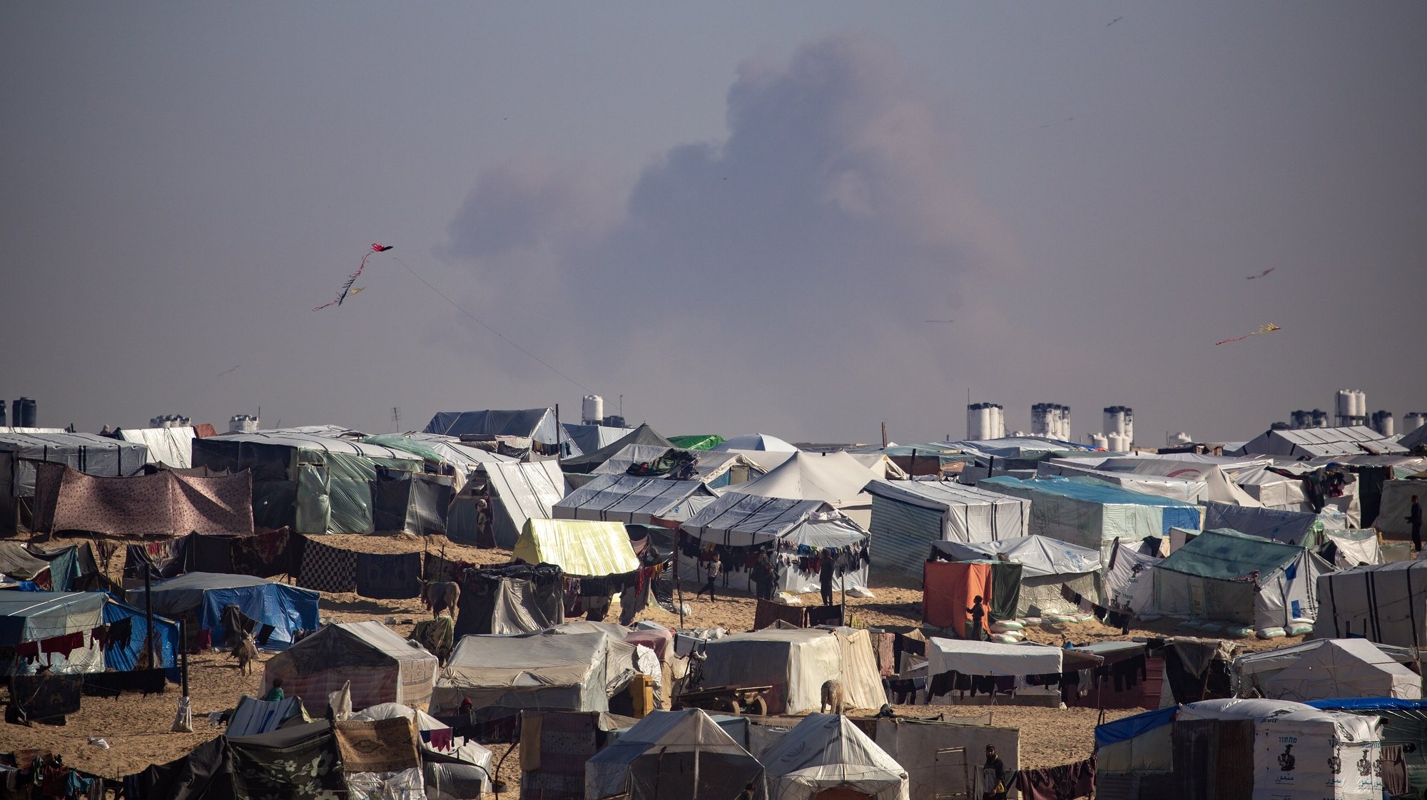 epaselect epa11136396 A camp of internally displaced Palestinians at the Gaza border with Egypt, while smoke rises from an Israeli air strike, in the Rafah refugee camp, southern Gaza Strip, 08 February 2024. Since 07 October 2023, up to 1.9 million people, or more than 85 percent of the population, have been displaced throughout the Gaza Strip, some more than once, according to the United Nations Relief and Works Agency for Palestine Refugees in the Near East (UNRWA), which added that most civilians in Gaza are in &#039;desperate need of humanitarian assistance and protection&#039;.  EPA/HAITHAM IMAD