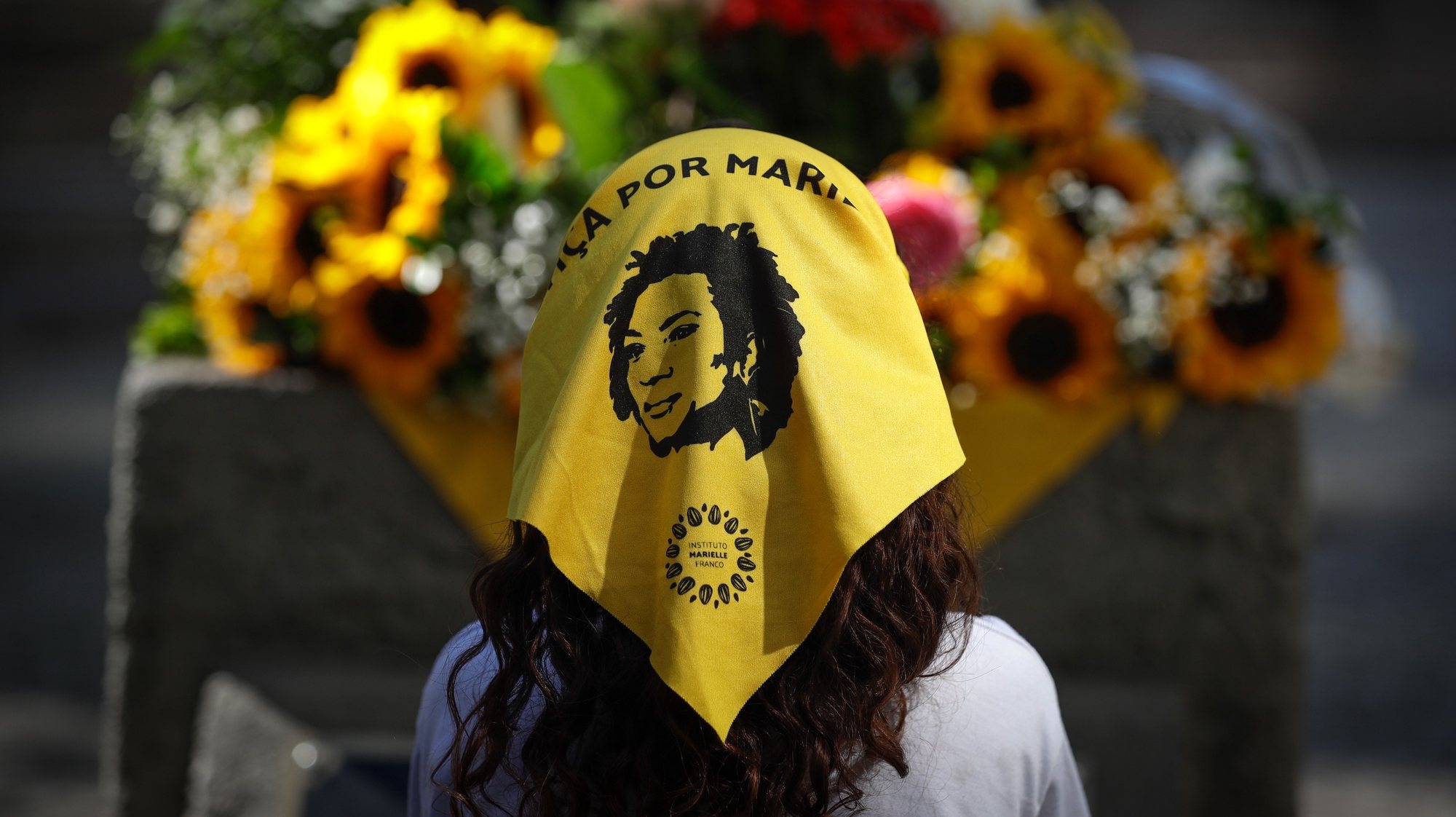 epa10771944 A girl wears a scarf with the phrase &#039;Justice for Marielle&#039; in front of flowers placed at the foot of the statue of councilwoman Marielle Franco, during an act in her honor in Rio de Janeiro, Brazil, 27 July 2023. On the day she would have turned 44, relatives of Brazilian councilwoman Marielle Franco commemorated her birth with a cultural day, amid recent advances in investigations on her case. Black, raised in a favela, lesbian and human rights defender, Marielle Franco was shot dead along with her driver, Anderson Torres, on the night of 14 March 2018 as they were leaving a political event in downtown Rio de Janeiro.  EPA/Andre Coelho