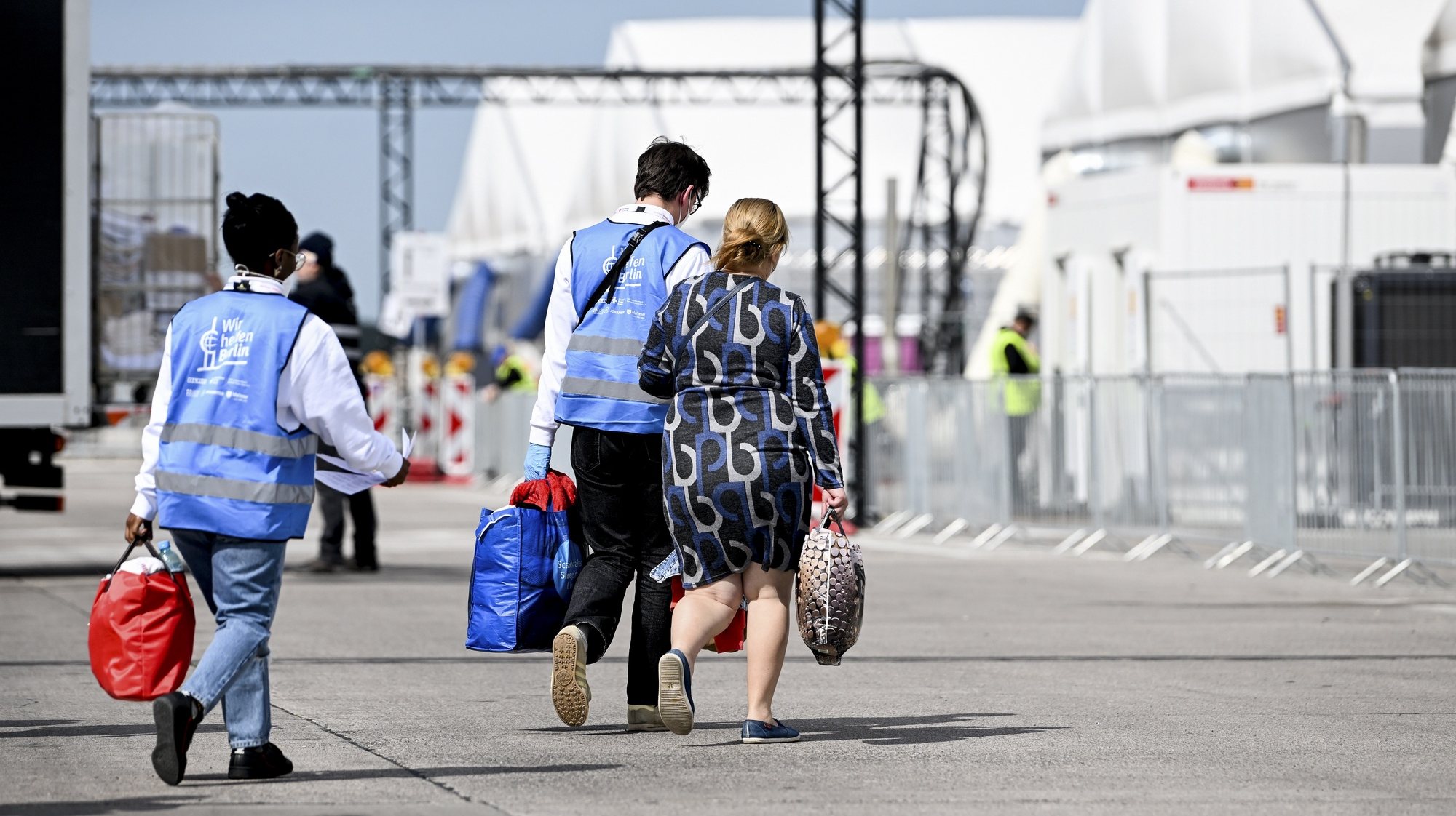 epa10638804 Workers help a woman with her luggage as she arrives at the centre for Ukrainian refugees, at the former Berlin Tegel Airport, in Berlin, Germany, 19 May 2023. The German Red Cross (DRK) has set up an arrival center for refugees in response to their massive arrival in Germany, at the beginning of the Ukrainian crisis in March 2022.  EPA/FILIP SINGER