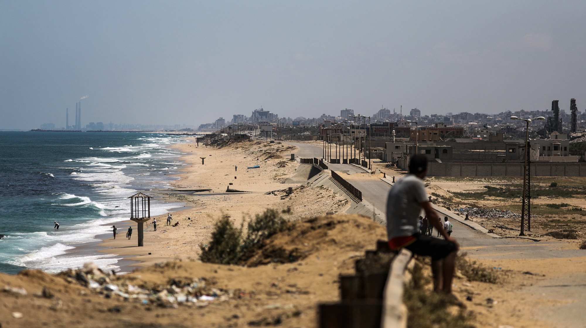 epa11377014 A Palestinian man sits on a guardrail along a road leading to the location of a temporary floating pier previously anchored by the United States to boost aid deliveries, in the northern Gaza Strip, 29 May 2024. The US Defense Department’s spokesperson confirmed on 28 May that the pier had been damaged by ‘an unfortunate confluence of weather storms’ and that it would be operational again in little over a week after repair work.  EPA/MOHAMMED SABER