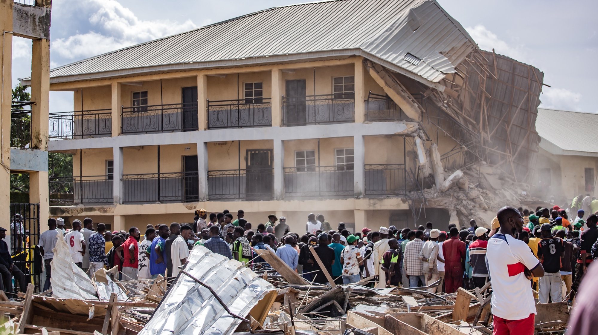 epa11474926 People gather at the site of a collapsed building at Saint Academy school in Jos North, district of Plateau State, Nigeria, 12 July 2024. Nigeria’s National Emergency Management Agency (NEMA) reported that at least 16 students have died and several others have been trapped when a two storey building housing a school partially collapsed while exams were being held.  EPA/BECKY RENNISTORIES