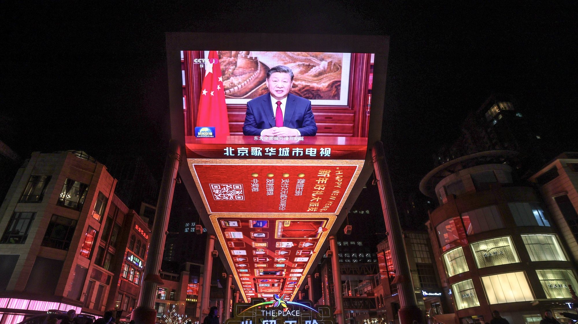 epa11050285 People walk past a screen that shows Chinese President Xi Jinping delivering a New Year address to ring in 2024, in Beijing, China, 31 December 2023.  EPA/WU HAO