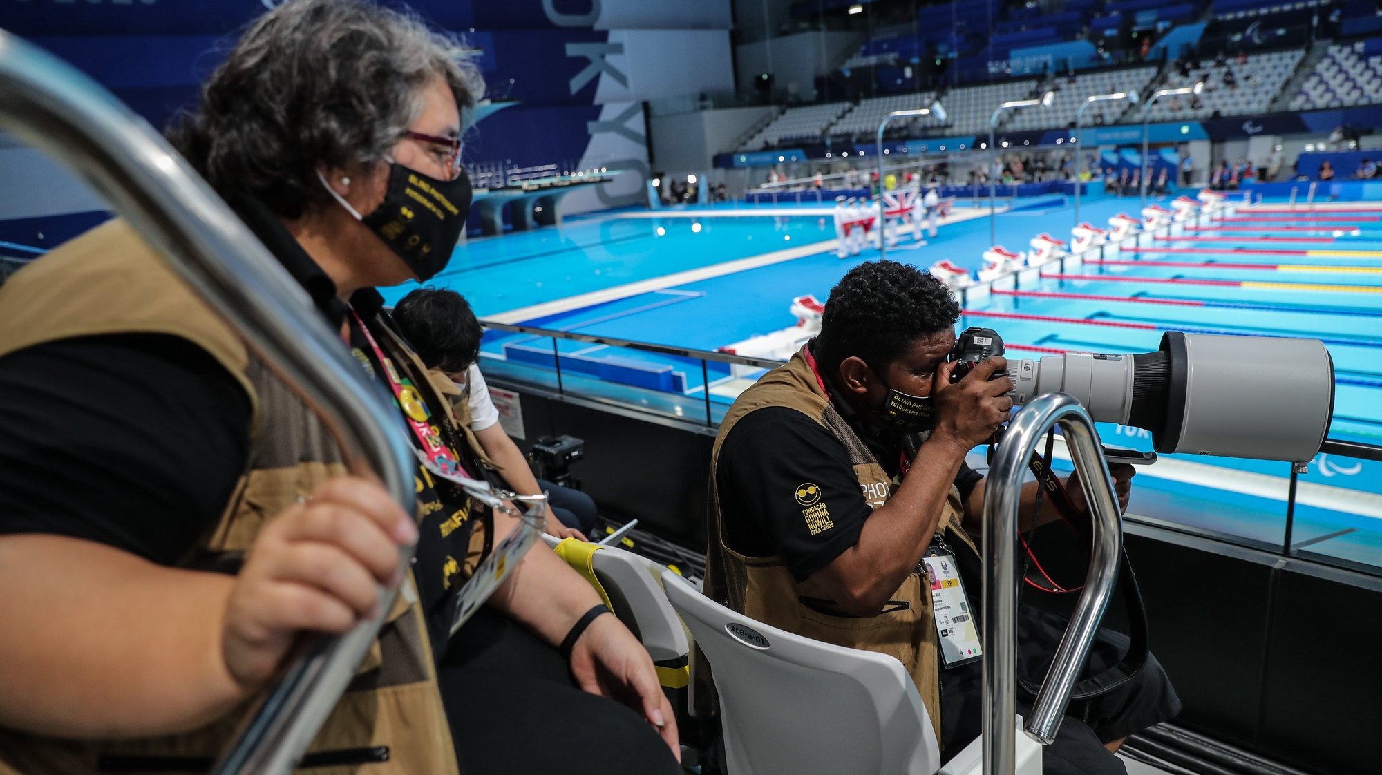 O fotógrafo Brasileiro João Maia (D), acompanhado pela sua guia e tradutora, Sandra Chammem (E), fotografa uma prova de natação no Centro Aquático de Tóquio, nos jogos Paralímpicos de Tóquio2020, Japão, 28 de agosto de 2021. (ACOMPANHA TEXTO DE 2 DE SETEMBRO DE 2021). MIGUEL A. LOPES/LUSA