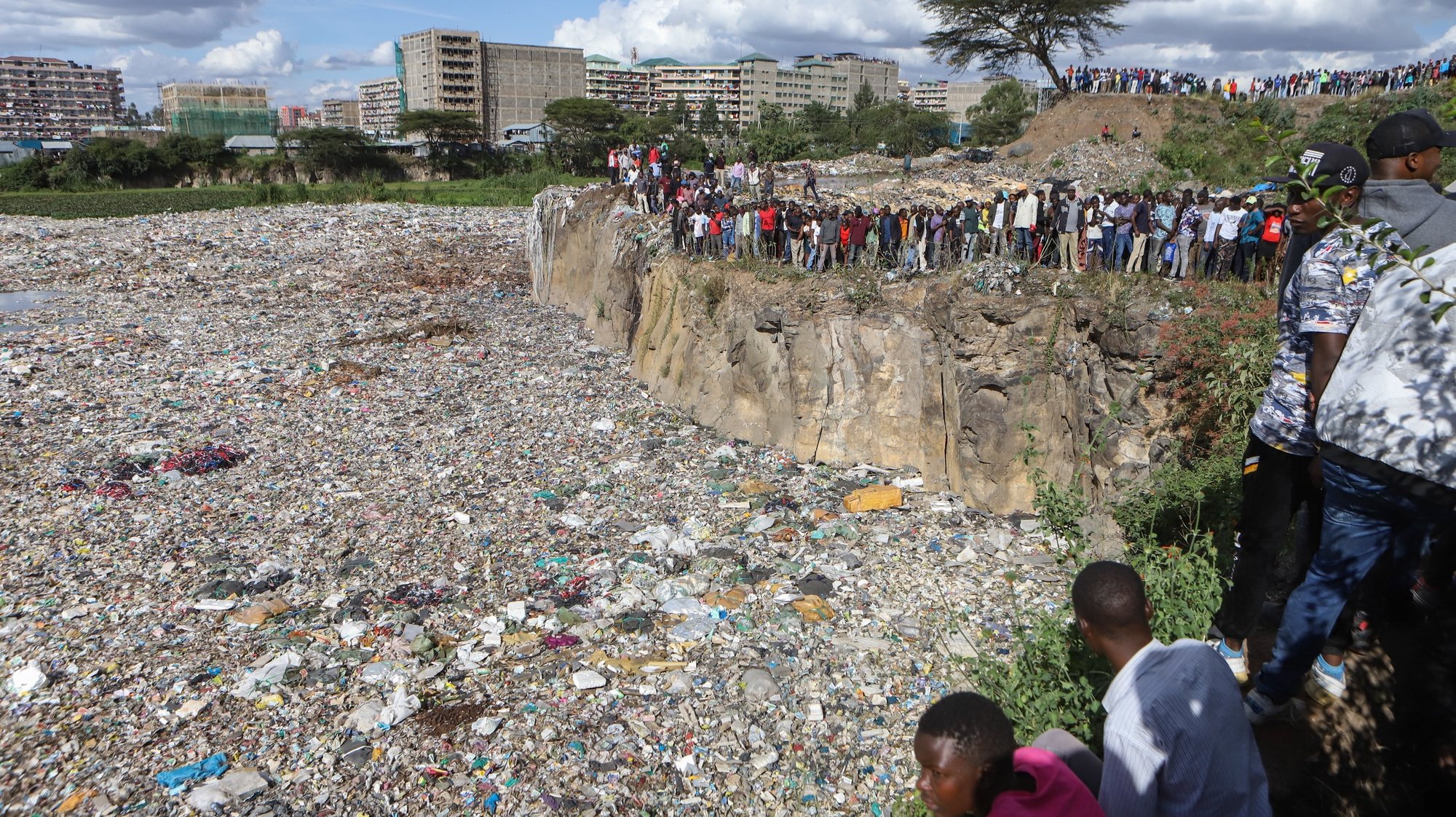 epa11474629 Onlookers watch as bodies wrapped in bags are being retrieved from inside a quarry turned into a dump site at Embakasi area in Nairobi, Kenya, 12 July 2024. Police stated that six severely mutilated female bodies, in various stages of decomposition and wrapped in nylon bags and ropes, were recovered from the former quarry near Mukuru Kwa Njenga slum in Nairobi. Police said the area has been declared a crime scene and an investigation is underway.  EPA/STRINGER