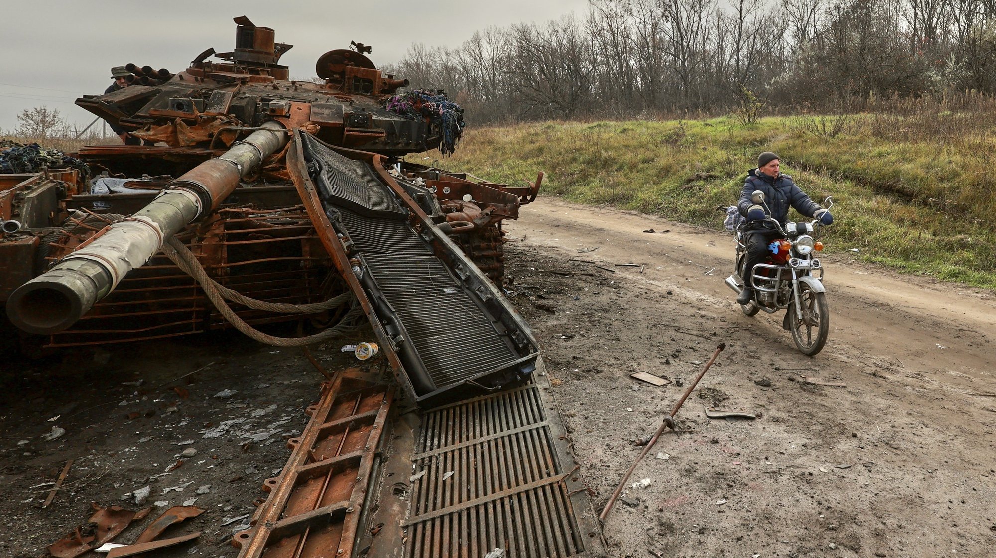 epa10296694 A local man rides a motor bike past a destroyed tank in the Kharkiv region, Ukraine, 09 November 2022. A counter-offensive by Ukrainian forces led to the withdrawal of Russian troops who occupied territory in the northeast of the country. Kharkiv and surrounding areas have been the target of heavy shelling since February 2022, when Russian troops entered Ukraine starting a conflict that has provoked destruction and a humanitarian crisis.  EPA/SERGEY KOZLOV