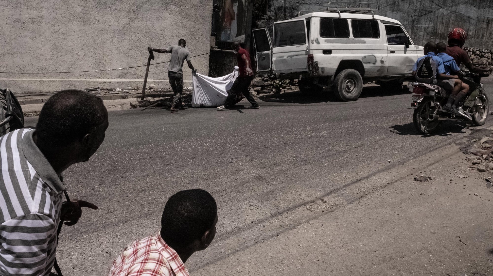 epaselect epa10605582 People look on as two men carry the cremated body of a person in Port-au-Prince, Haiti, 02 May 2023. At least five people were killed on 02 May 2023 by the population in Petion-ville, Port-au-Prince, for being alleged members of the Ti Makak armed group, dismantled a few weeks ago by the National Police.  EPA/Johnson Sabin