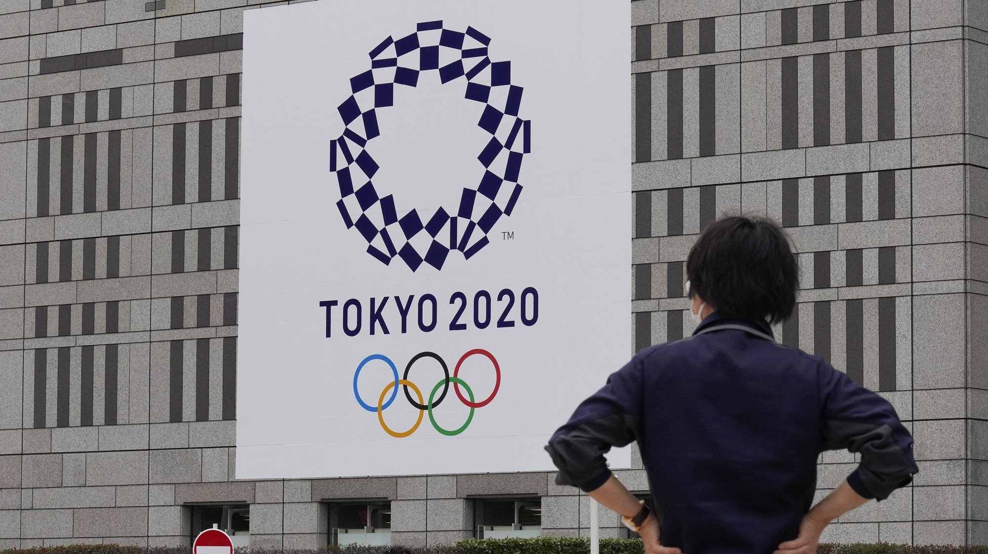 epa09293039 Pedestrians walk past the logo of the Tokyo 2020 Olympic Games decorated on the wall of Tokyo Metropolitan Government office building, Japan, 22 June 2021. Tokyo and Japan will mark one month before the opening of the Tokyo 2020 Olympic Games on 23 June 2021. The Summer Games was rescheduled from 2020 due to COVID-19 Coronavirus pandemic.  EPA/KIMIMASA MAYAMA