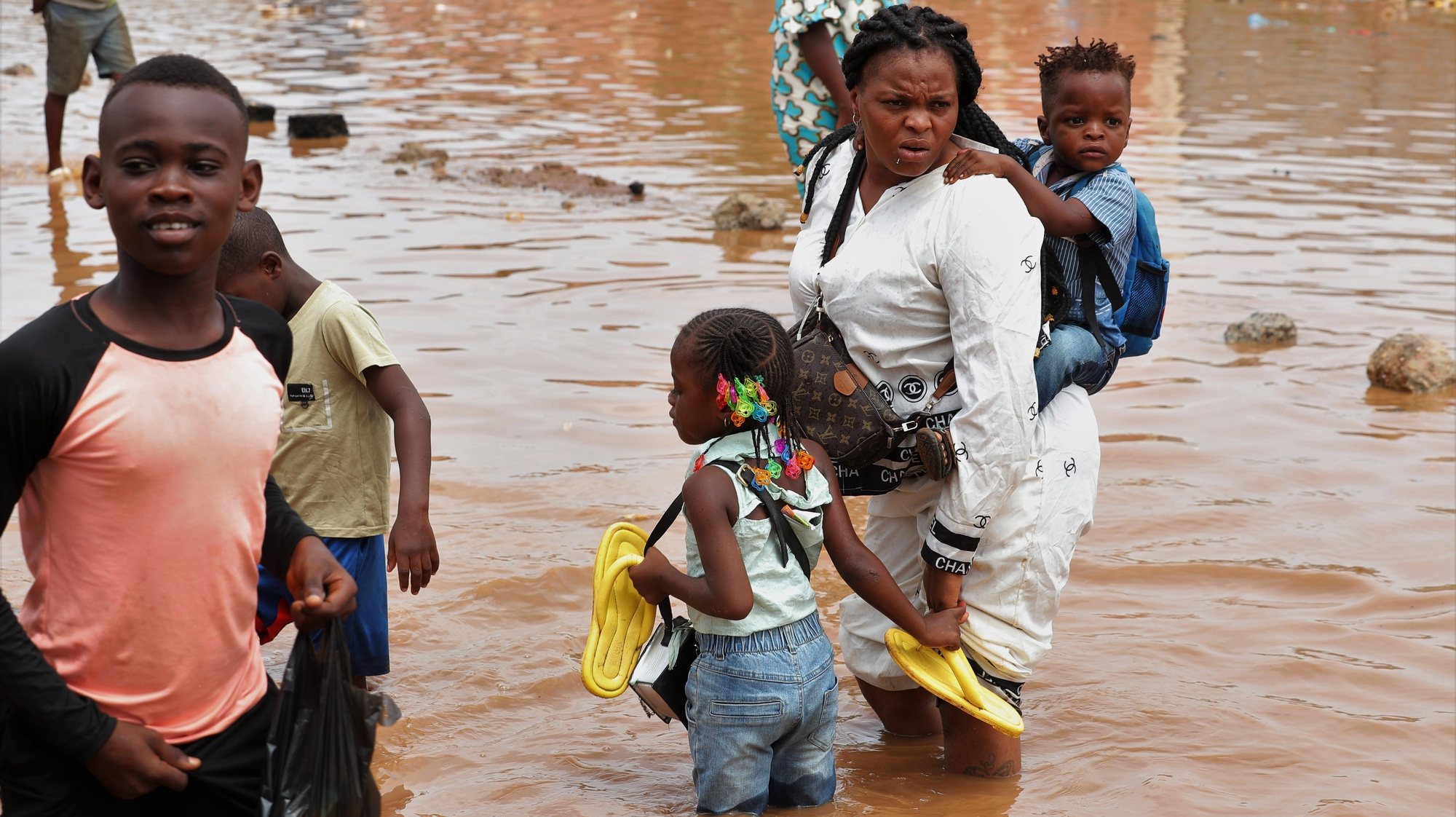epa10579117 Locals wade through flood waters caused by rainfall in Luanda, Angola, 18 April 2023. Since last week the rains that fell in Luanda area have caused the death of at least seven people, including three children in the early hours of 18 April, in addition to falling trees, thousands of flooded homes and collapsed electricity pylons.  EPA/AMPE ROGERIO