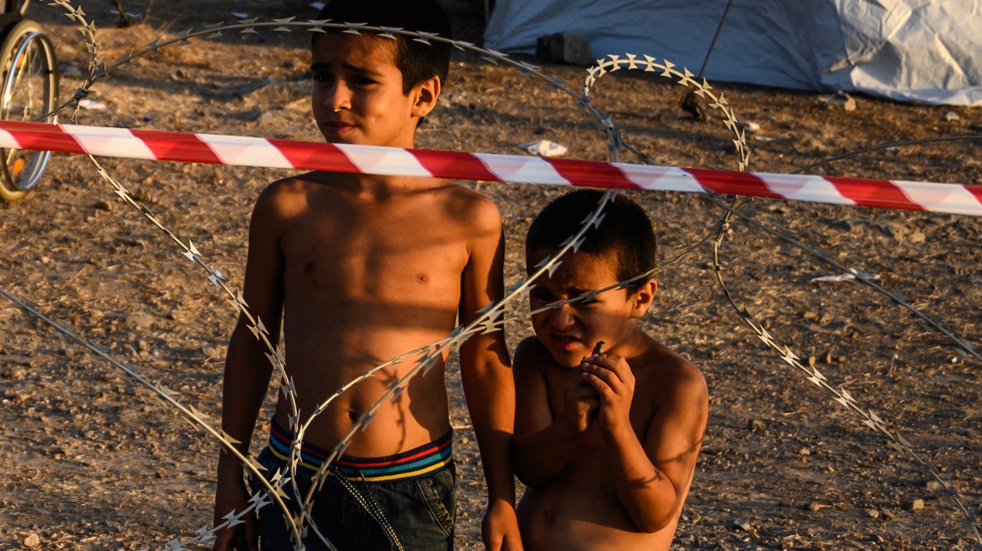 epa08682485 Two small boys stand behind razor wire at Kara Tepe camp on Lesbos island, Greece, 19 September 2020. Following the catastrophic fires at Moria on September 8 and 9, a total of 9,000 people were rehoused at the hotspot of Kara Tepe, south of Mytilini. All of them have been identified and their asylum applications are in process. Of them, 213 were found positive to the novel coronavirus and have been quarantined at separate quarters in the hotspot.  EPA/VANGELIS PAPANTONIS