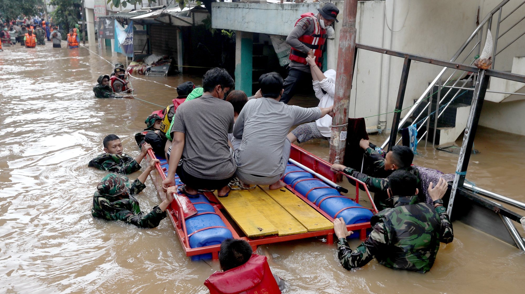 epaselect epa09025174 Indonesian military and police officers help a flood victim to get into a boat as they rescue residents in Jakarta, Indonesia, 20 February 2021. At least 21 areas flooded following heavy rains, during which thousands of homes were damaged in the capital, according to the National Board for Disaster Management (BNPB).  EPA/Bagus Indahono