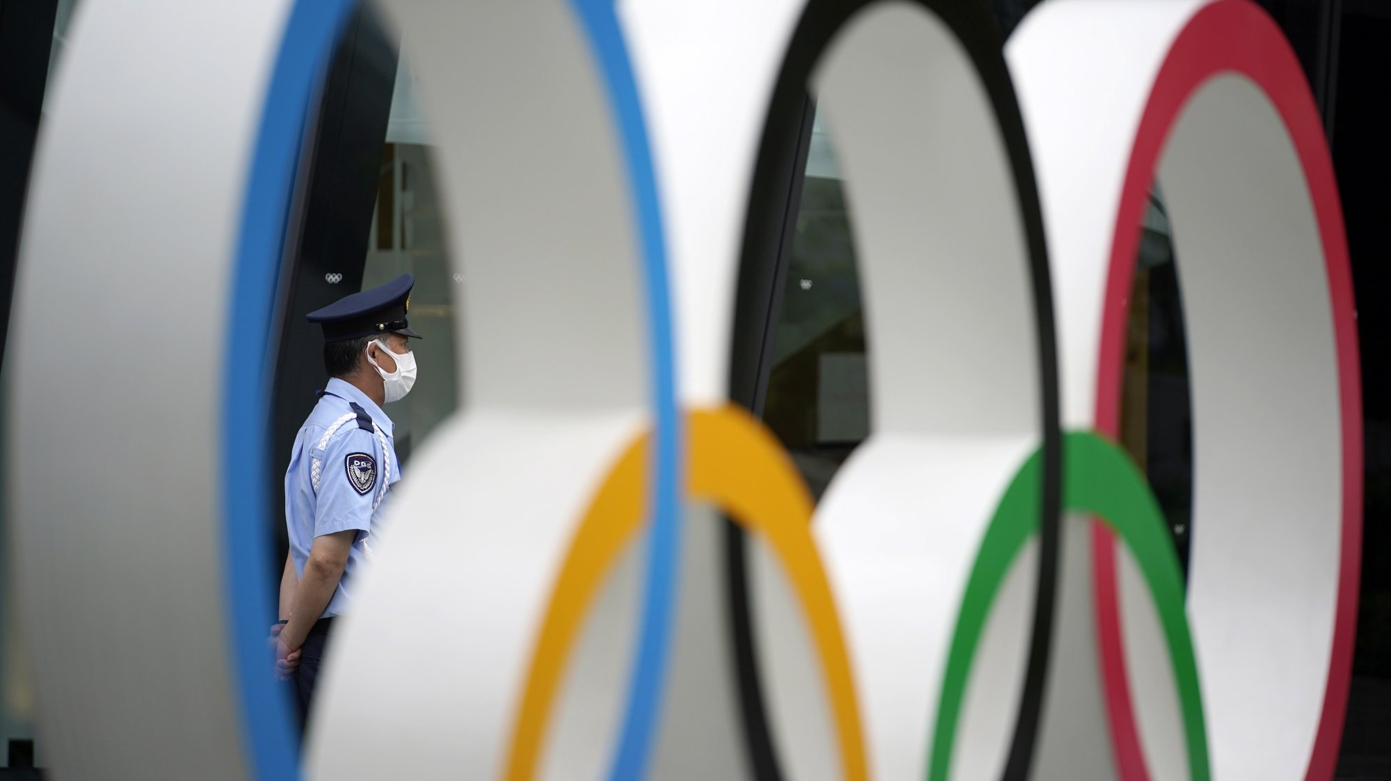 epa09293117 A security guard is seen through an Olympic Rings monument near the National Stadium, the main stadium of the 2020 Tokyo Olympic Games, in Tokyo, Japan, 22 June 2021. Tokyo will mark one month before the opening of the Tokyo 2020 Olympic Games on 23 June 2021. The Summer Games were postponed due to COVID-19 Coronavirus pandemic.  EPA/FRANCK ROBICHON