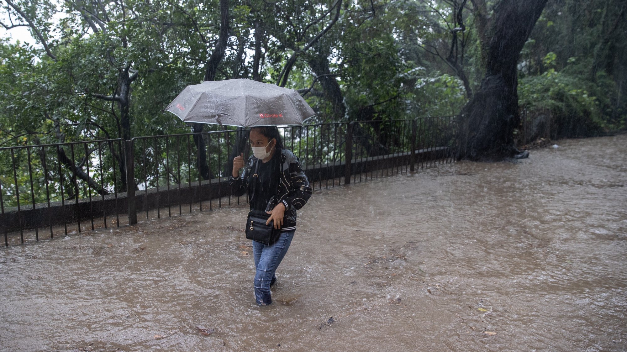 epa09512550 A woman makes her way in a road flooded by rain brought by tropical storm Lionrock in Hong Kong, China, 08 October 2021. The Hong Kong Observatory briefly upgraded its rainstorm warning to black, the highest level, amid torrential downpours brought by tropical storm Lionrock this morning.  EPA/JEROME FAVRE