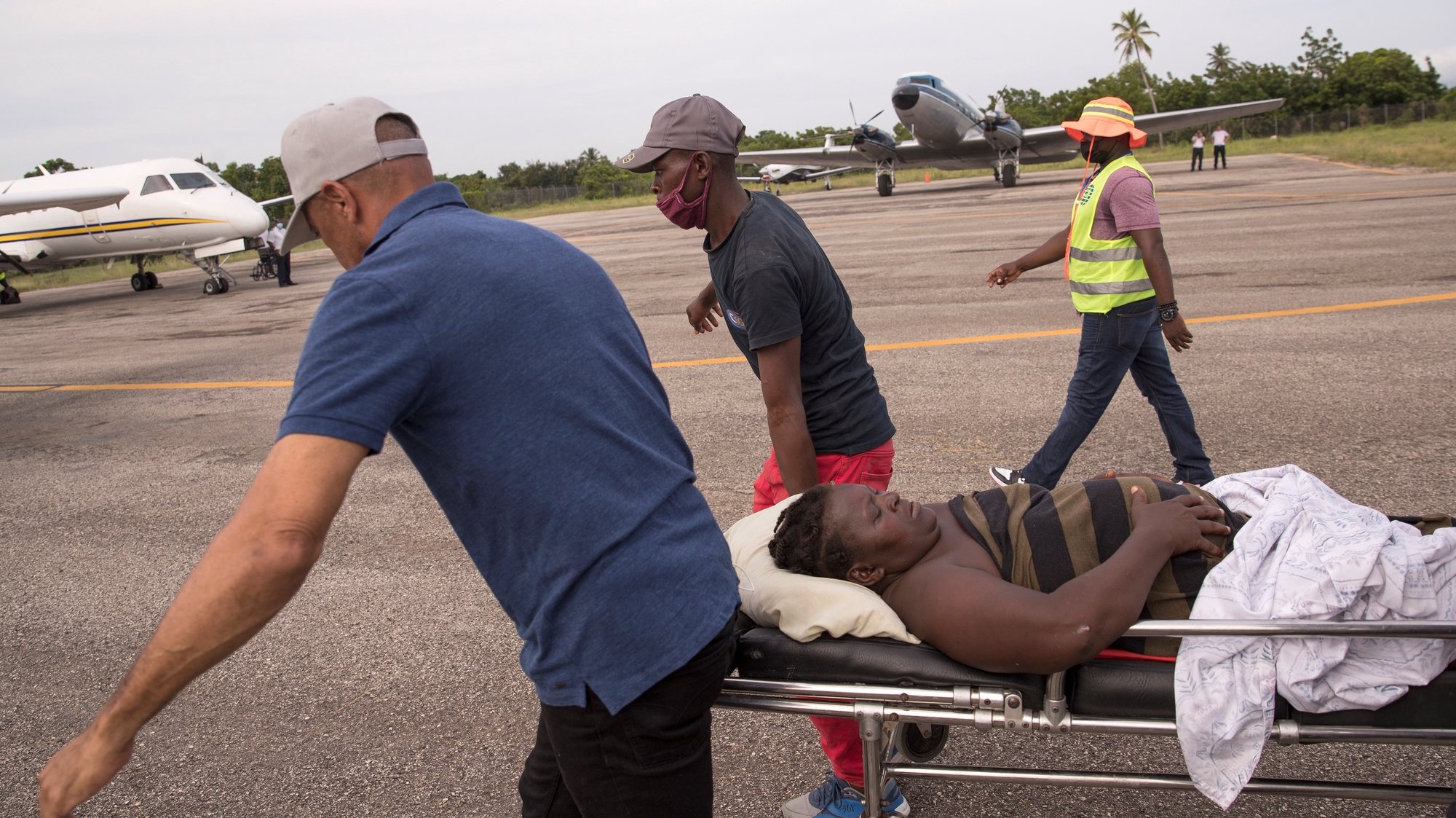 epa09420689 Some men carry a woman injured during the earthquake on a stretcher to be transferred by plane to a hospital in Port-au-Prince, from Les Cayes, Haiti, 19 August 2021. At least 2,189 people died and 12,268 were injured as a result of the 7.2 earthquake that devastated much of southern Haiti on August 14, in addition to substantial material losses, according to the latest official count.  EPA/ORLANDO BARRIA