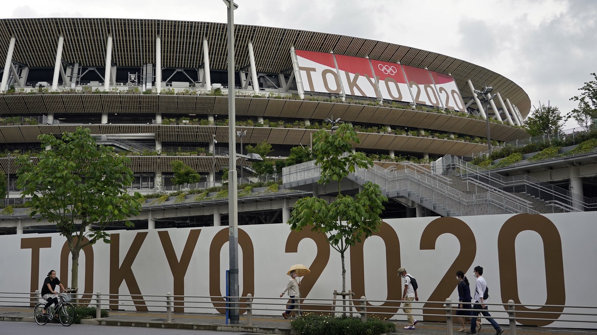 epa09294866 Passersby walk past the National Stadium, the main stadium of the 2020 Tokyo Olympic Games, in Tokyo, Japan, 23 June 2021, one month before the opening of the Tokyo 2020 Olympic Games. The National Stadium will host the opening, closing ceremonies and the athletics events. The Summer Games were postponed due to COVID-19 Coronavirus pandemic.  EPA/FRANCK ROBICHON