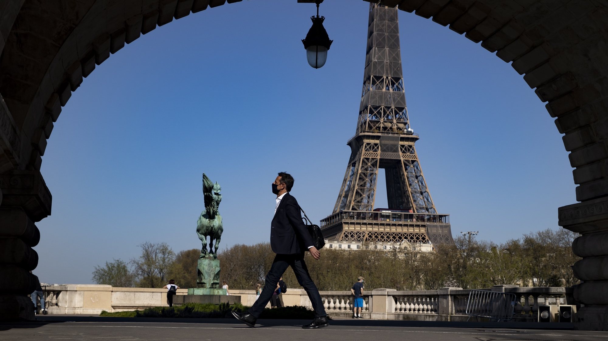 epa09108792 A Pedestrian wearing protective face mask enjoys the warm spring weather walking across the Bir Hakeim bridge near the Eiffel Tower, hours before French President Emmanuel Macron is due to make a televised address to the nation to announce enhanced measures to fight the spread of Covid19 coronavirus as France faces a third wave of the pandemic,  in Paris, France, 31 March 2021.  EPA/IAN LANGSDON
