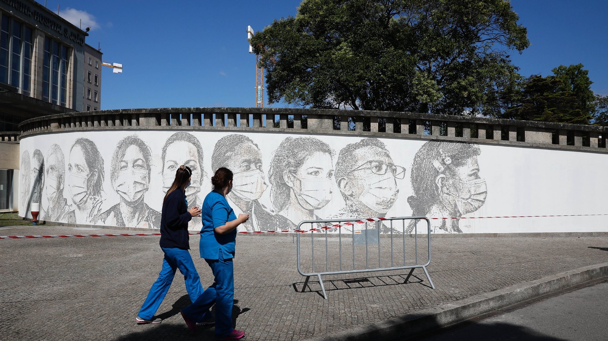 Two health workers pass by a mural with ten faces as a tribute to all health workers carved by Portuguese street artist Alexandre Farto, tag-named as VHILS, are seen at Sao Joao Hospital in Porto, Portugal, 19 June 2020. JOSE COELHO/LUSA