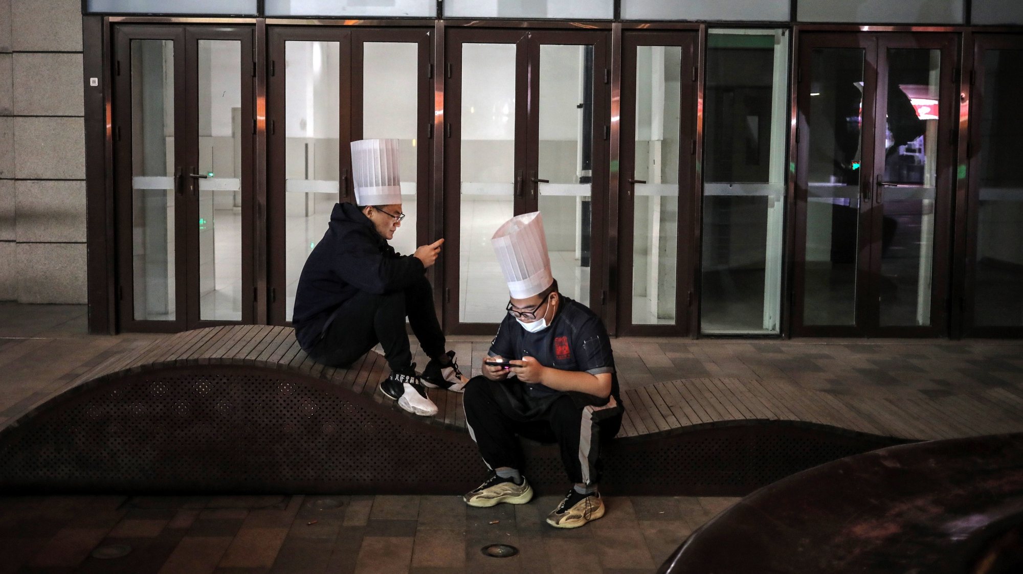 epa08899396 Two chefs use their mobile phones outside a shopping mall in Beijing, China, 22 December 2020.  EPA/WU HONG
