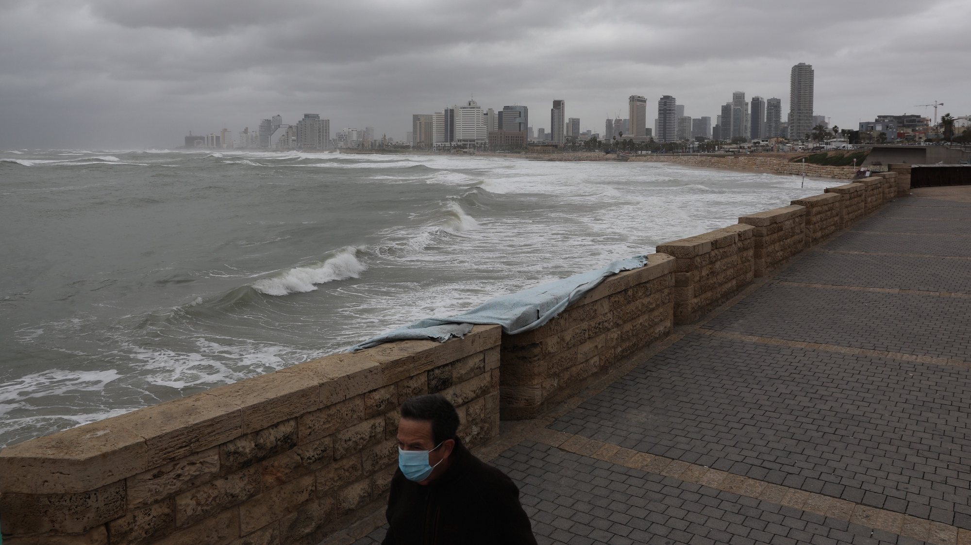 epa08948555 A man wearing a face mask walks along an empty promenade during a full lockdown at a beach in Tel Aviv, Israel, 19 January 2021. Although Israel is one of the first countries to have received vaccines and has so far vaccinated more than two million of its around nine million citizens, the rate of infection with the Sars-CoV-2 coronavirus that causes the coronavirus disease (COVID-19), is rising as Israel entered a full closure of two weeks.  EPA/ABIR SULTAN