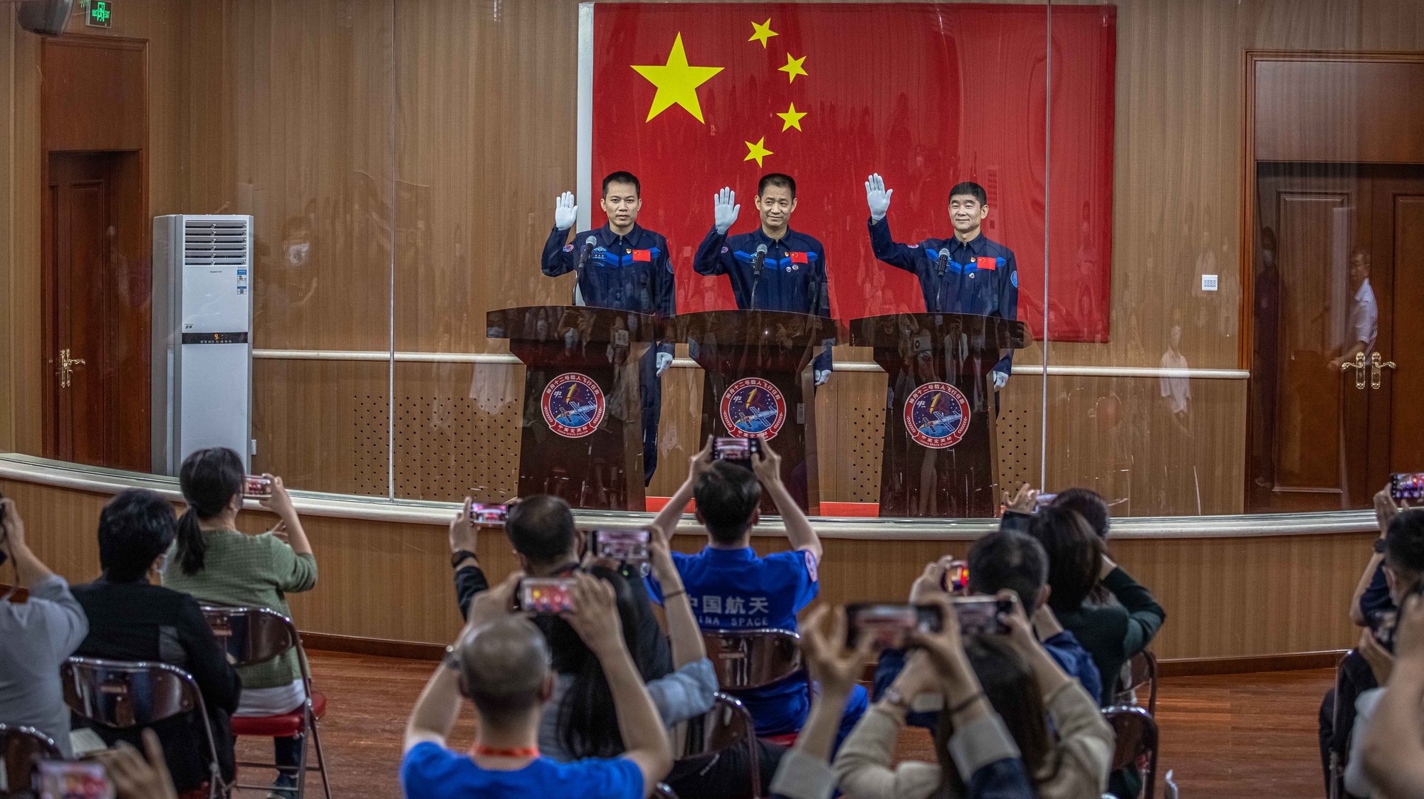 epaselect epa09275128 Chinese astronauts (L-R) Tang Hongbo, Nie Haisheng, and Liu Boming wave during a press conference at the Jiuquan Satellite Launch Center, the day before the launching of the Long March-2F carrier rocket, carrying the Shenzhou-12, in northwestern Gansu province, China, 16 June 2021. China will launch the Shenzhou-12 spacecraft carrying three crew members to the orbiting Tianhe core module for a three-month mission on 17 June. It is the first spaceflight in almost five years when China sends humans into space.  EPA/ROMAN PILIPEY