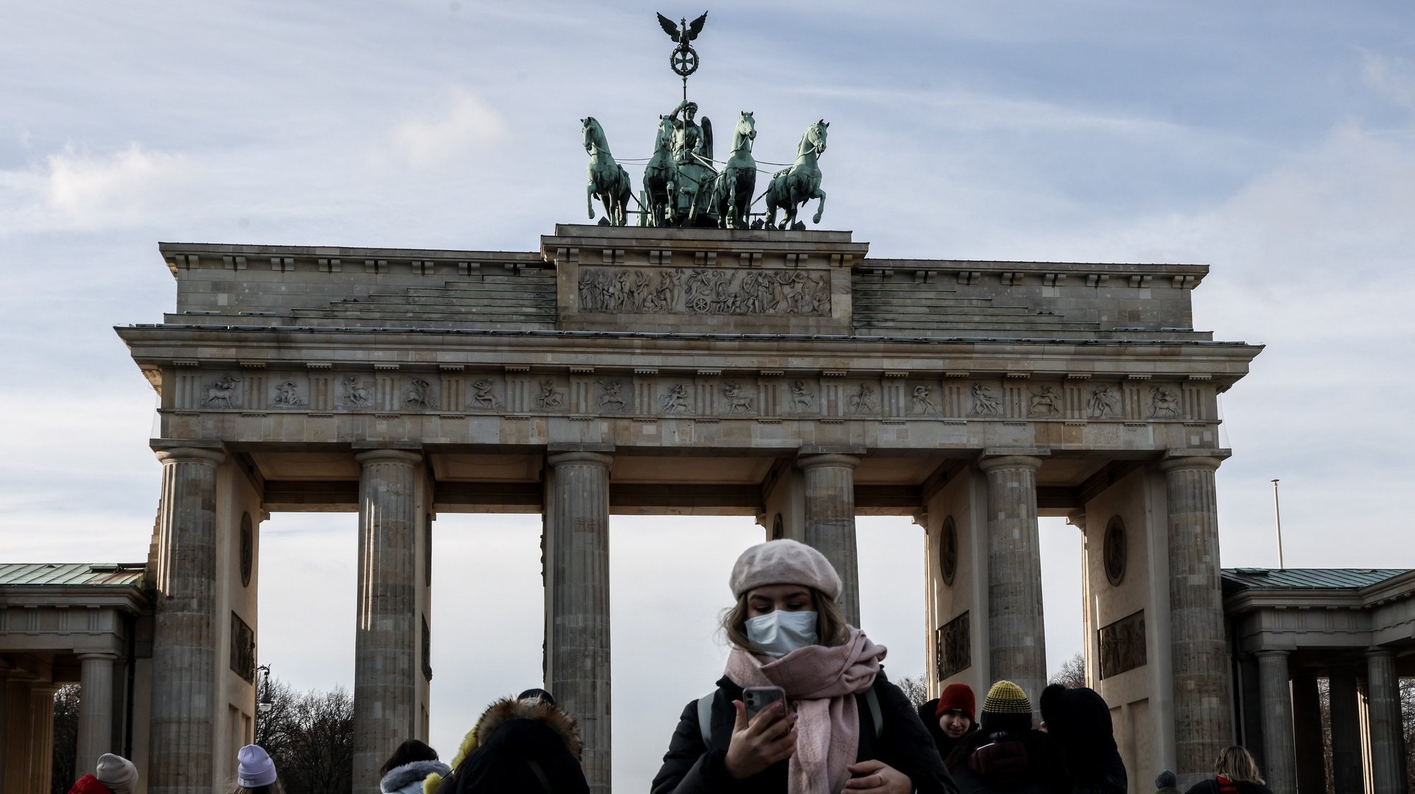 epa09619354 A woman wears a face mask in-front of the Brandenburg Gate in Berlin, Germany, 03 December 2021. Germany is dealing with a rising number of new coronavirus COVID-19 infections as countries throughout Europe have been increasing restrictions amid fear of the new Omicron variant of concern.  EPA/FILIP SINGER