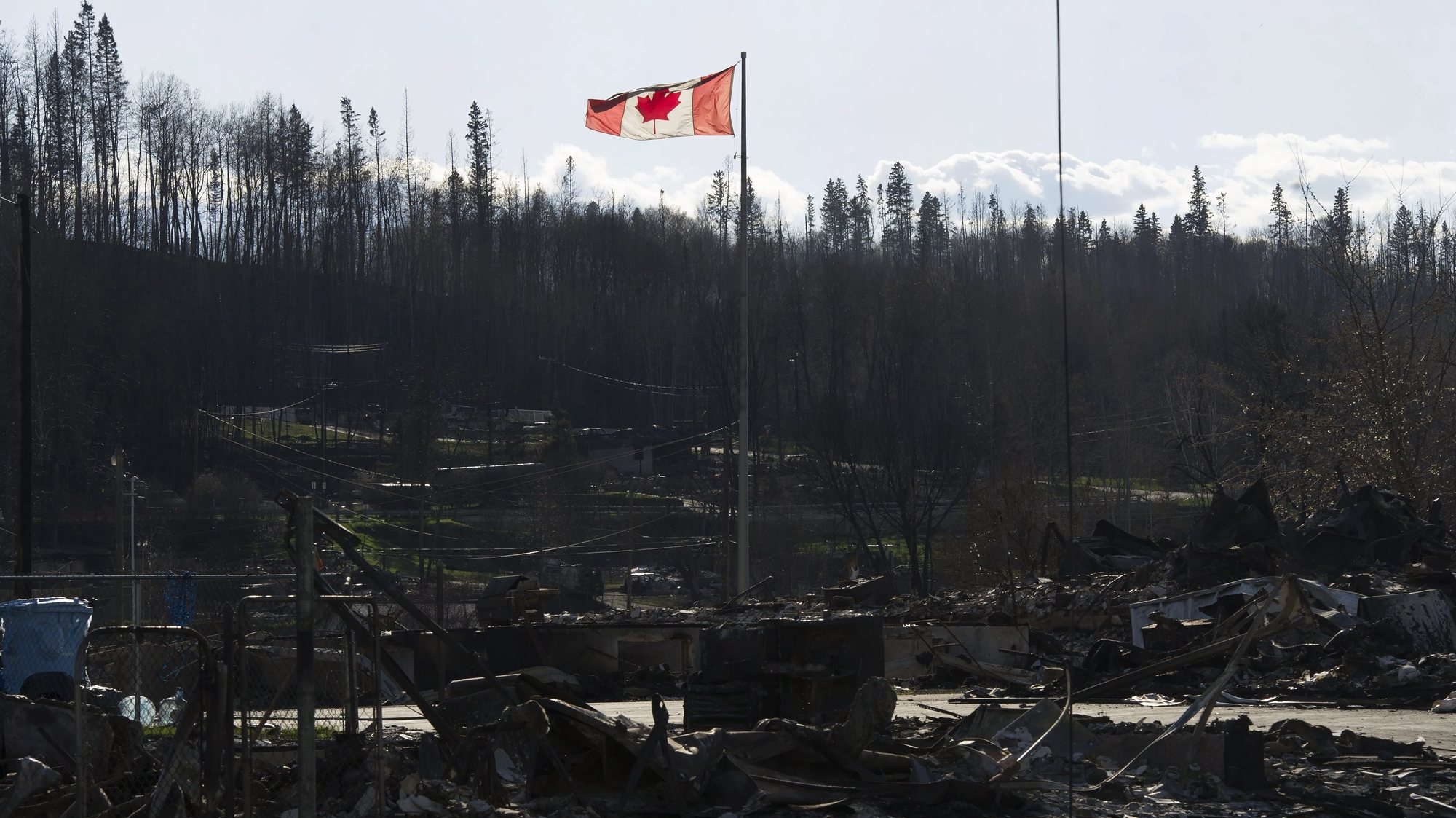 epa05309303 A handout picture made available by the Government of Alberta on 16 May 2016 shows a Canadian national flag flying over a general view of damage caused by a wildfire that swept through several neighbourhoods in Fort McMurray, Alberta, Canada, 14 May 2016. Alberta Health Services has issued an air-quality advisory for the Fort McMurray area. A wildfire erupted on 03 May destroying the city of Fort MacMurray, and forcing more than 88,000 people to evacuate from the area, leaving more than 200,000 hectares burnt. Government officials say that only heavy rain would extinguish the fire.  EPA/GOVERNMENT OF ALBERTA/CHRIS SCHWARZ  HANDOUT EDITORIAL USE ONLY