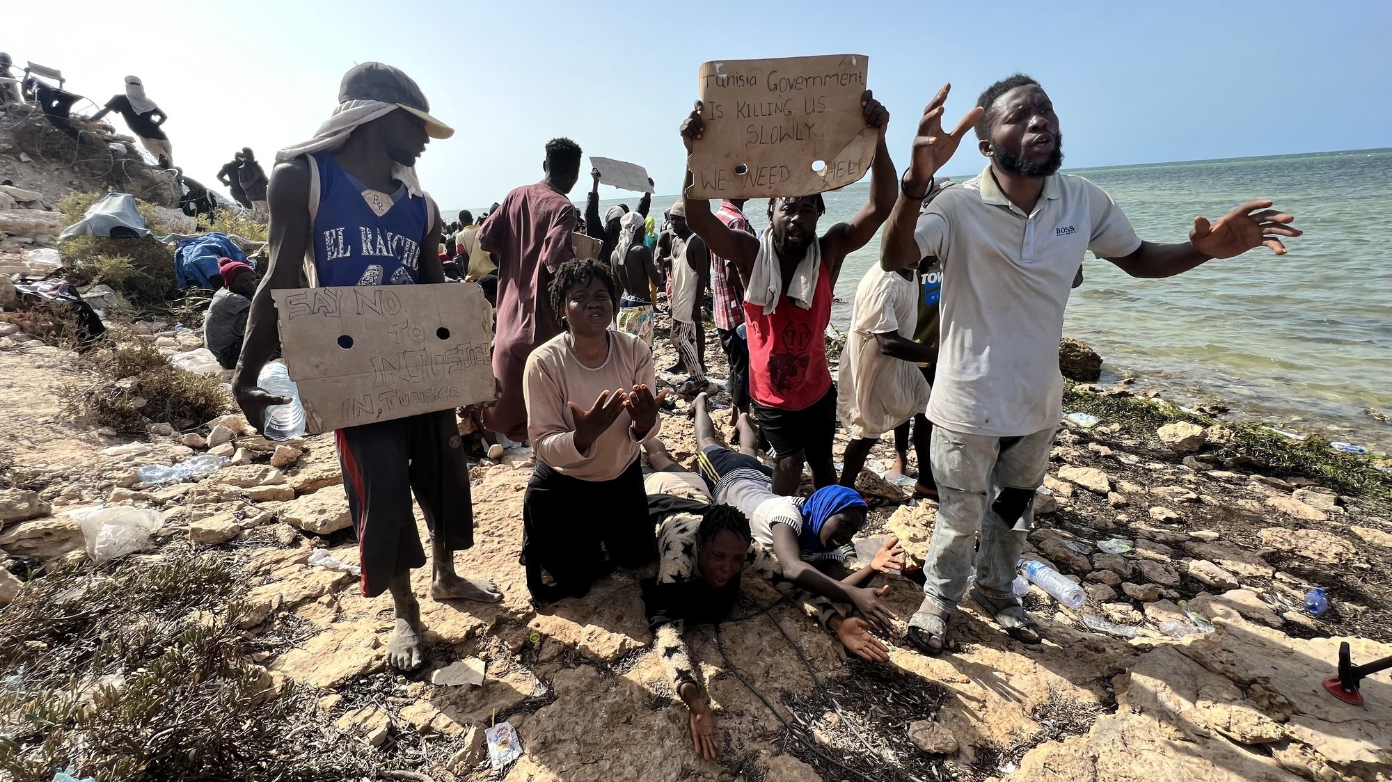 epa10770022 Sub-Saharan African migrants who were expelled from the city of Sfax in Tunisia beg for help as they gather in an area near the Libyan-Tunisia border, in Ras Jedir, 173 km west of Tripoli, Libya, 26 July 2023. Libyan border guards found some 150 people, women, children and families stranded in scorching summer temperatures and without water. According to the Red Crescent, Tunisian security forces have moved hundreds of migrants into the arid zone since June 2023.  EPA/STR