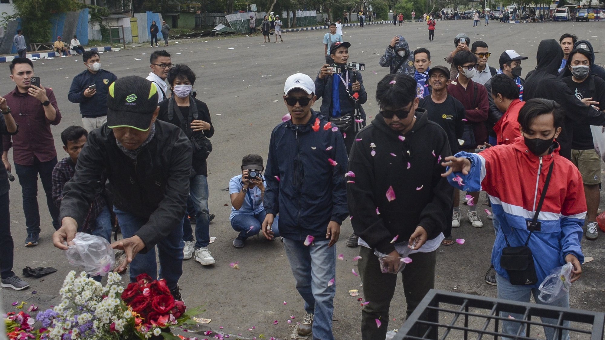 epa10219392 Local soccer club fans throw flowers as they pay condolences to the victims of the soccer match riot and stampede outside Kanjuruhan Stadium in Malang, East Java, Indonesia, 02 October 2022. Indonesia&#039;s National Police Chief General Listyo Sigid Prabowo announced that at least 125 people, including police officers, were killed after Indonesian soccer fans entered the pitch causing panic and stampede, after the match between Arema FC and Persebaya Surabaya in East Java on 01 October. The Football Association of Indonesia temporarily suspended the 2022/2023 Liga 1 competition for one week, and prohibited Arema FC from hosting for the rest of the competition this season.  EPA/SANDI SADEWA