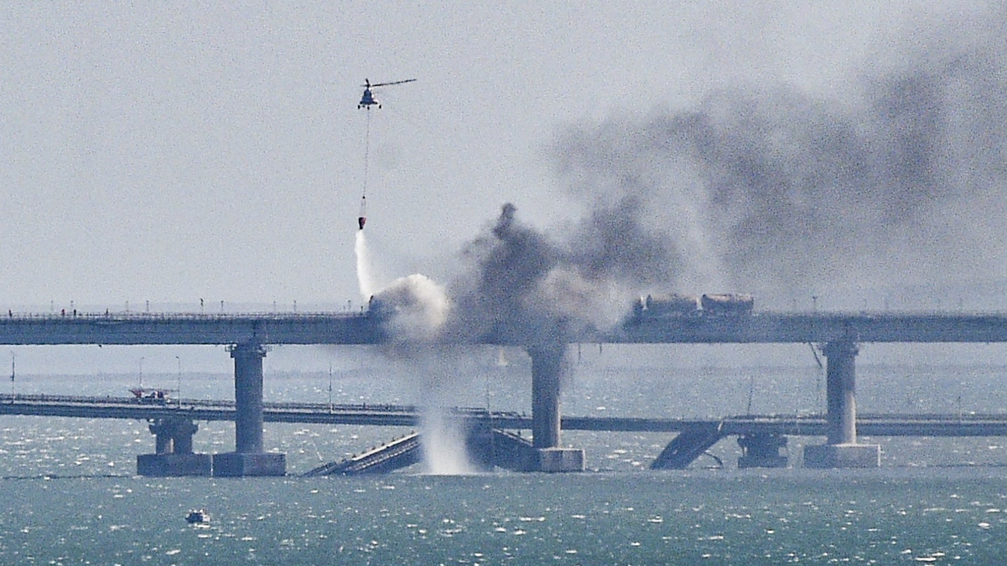 epaselect epa10230640 A firefighter helicopter pours water on fire on a collapsed part of the Kerch Strait bridge in Crimea, 08 October 2022. According to Russian authorities, &quot;an explosion was set off at a cargo vehicle on the motorway part of the Crimean bridge on the side of the Taman peninsula, which set fire to seven fuel tanks of a train that was en route to the Crimean peninsula. Two motorway sections of the bridge partially collapsed.&quot;  EPA/STRINGER