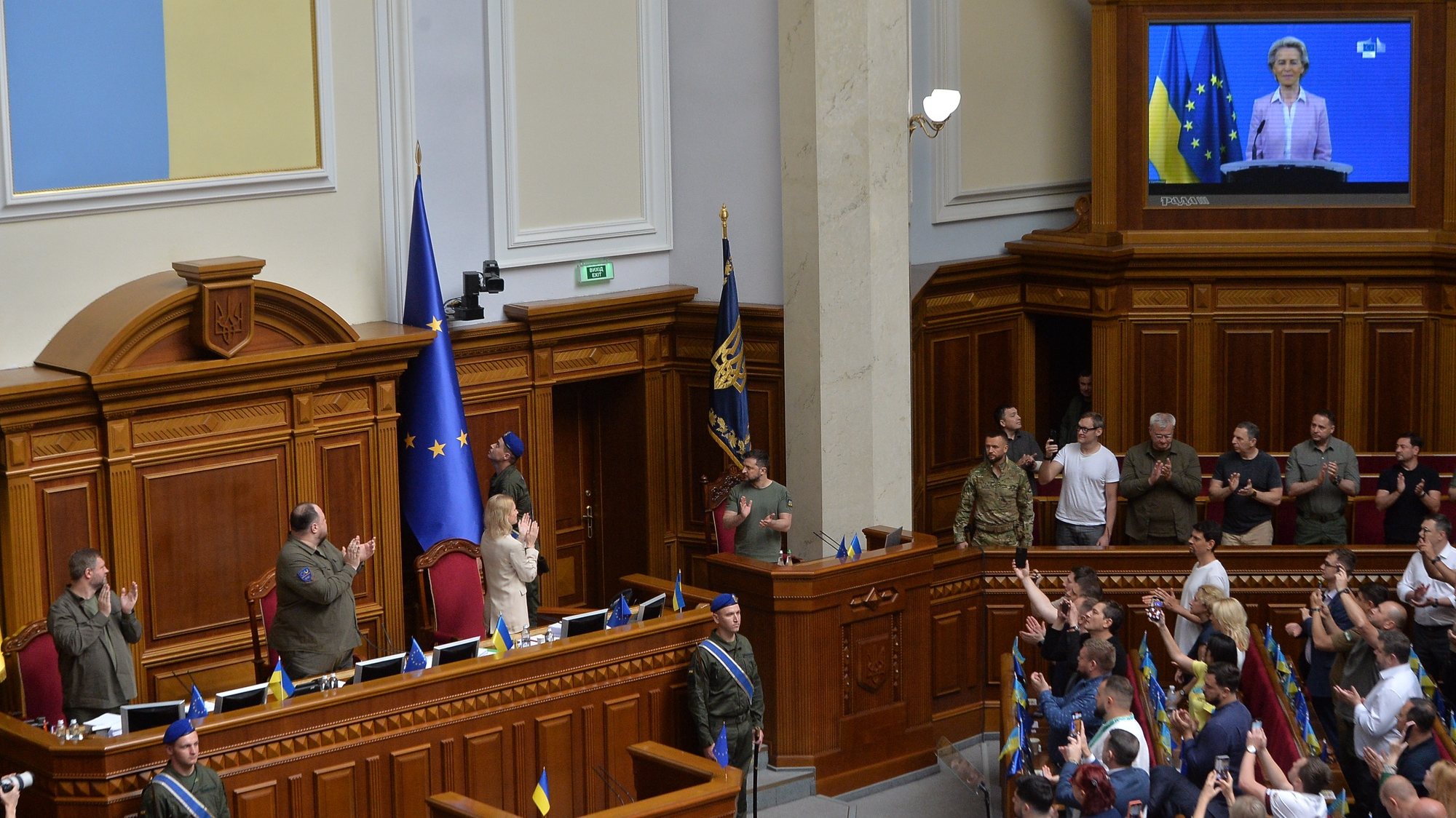 epa10045588 A Ukrainian serviceman raises the EU flag as European Commission President Ursula von der Leyen (on screen) remotely addresses Ukrainian deputies and Ukrainian President Volodymyr Zelensky (C) in the Verkhovna Rada (Ukrainian Parliament) in Kyiv, Ukraine, 01 July 2022. Ursula von der Leyen stated conditions as part of reforms that will bring the country into the European Union. The heads of state and government of the European Union at a summit in Brussels on June 23 approved granting Ukraine and Moldova the status of candidates for joining the union. To start accession negotiations, countries need to fulfil a number of conditions, including anti-corruption and judicial reforms, and strengthening the fight against oligarchs.  EPA/ANDRII NESTERENKO