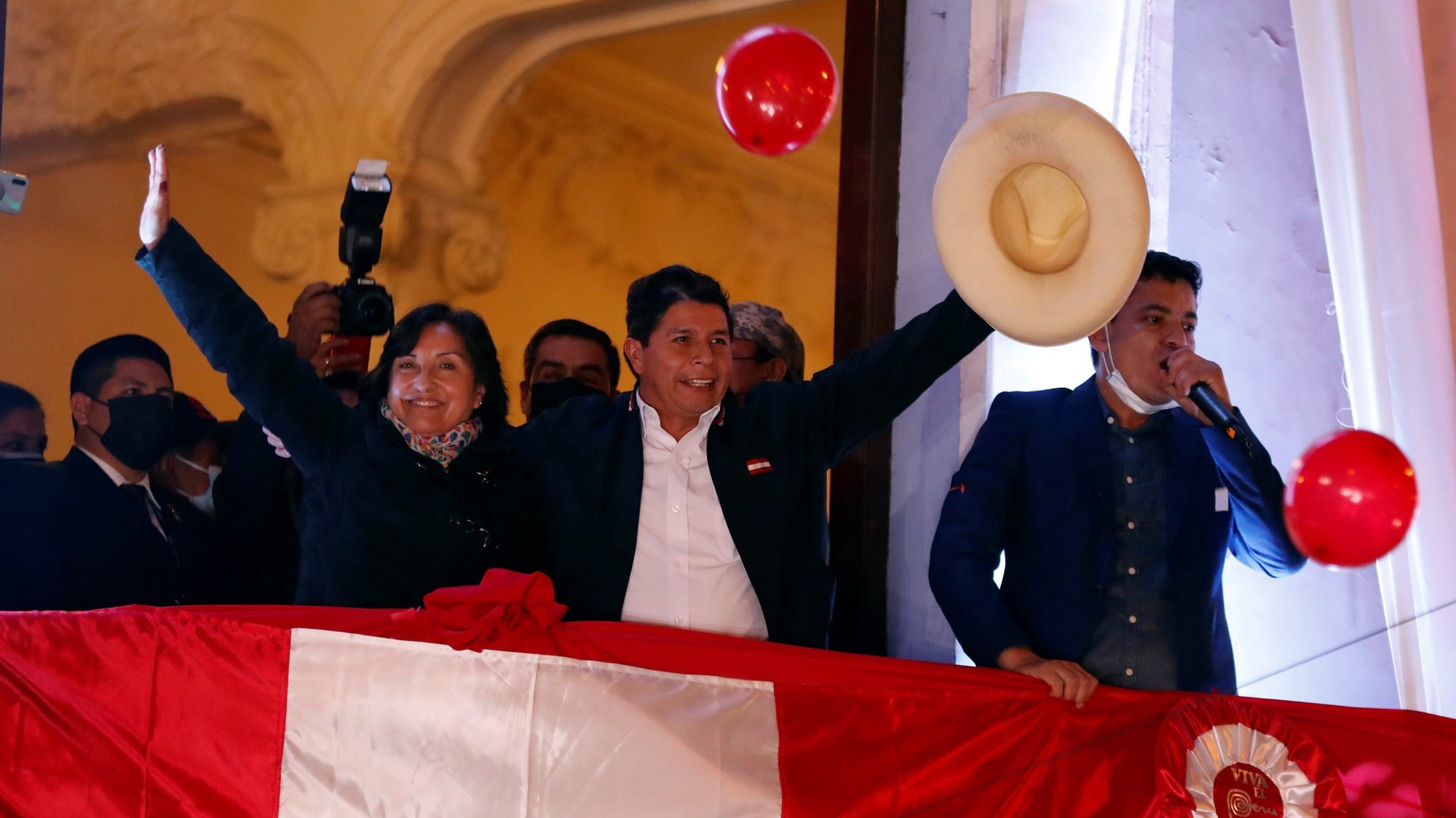 epa09353989 The leftist Pedro Castillo (C), accompanied by his formula to the Vice Presidency Dina Boluarte (L), greets supporters from a balcony after being proclaimed president-elect of the country, in Lima, Peru 19 July 2021. The official proclamation came this Monday, a month and a half after the elections in which he defeated the right-wing Keiko Fujimori, who delayed his appointment with more than a thousand challenges in which she denounced alleged &#039;fraud&#039; without reliable evidence. After declaring the latest legal appeals presented by Fujimori unfounded, the National Elections Jury (JNE) endorsed the results of the 06 June vote, where Castillo obtained 50.12% of the valid votes, a narrow victory by just 44,263 votes over Fujimori.  EPA/Paolo Aguilar