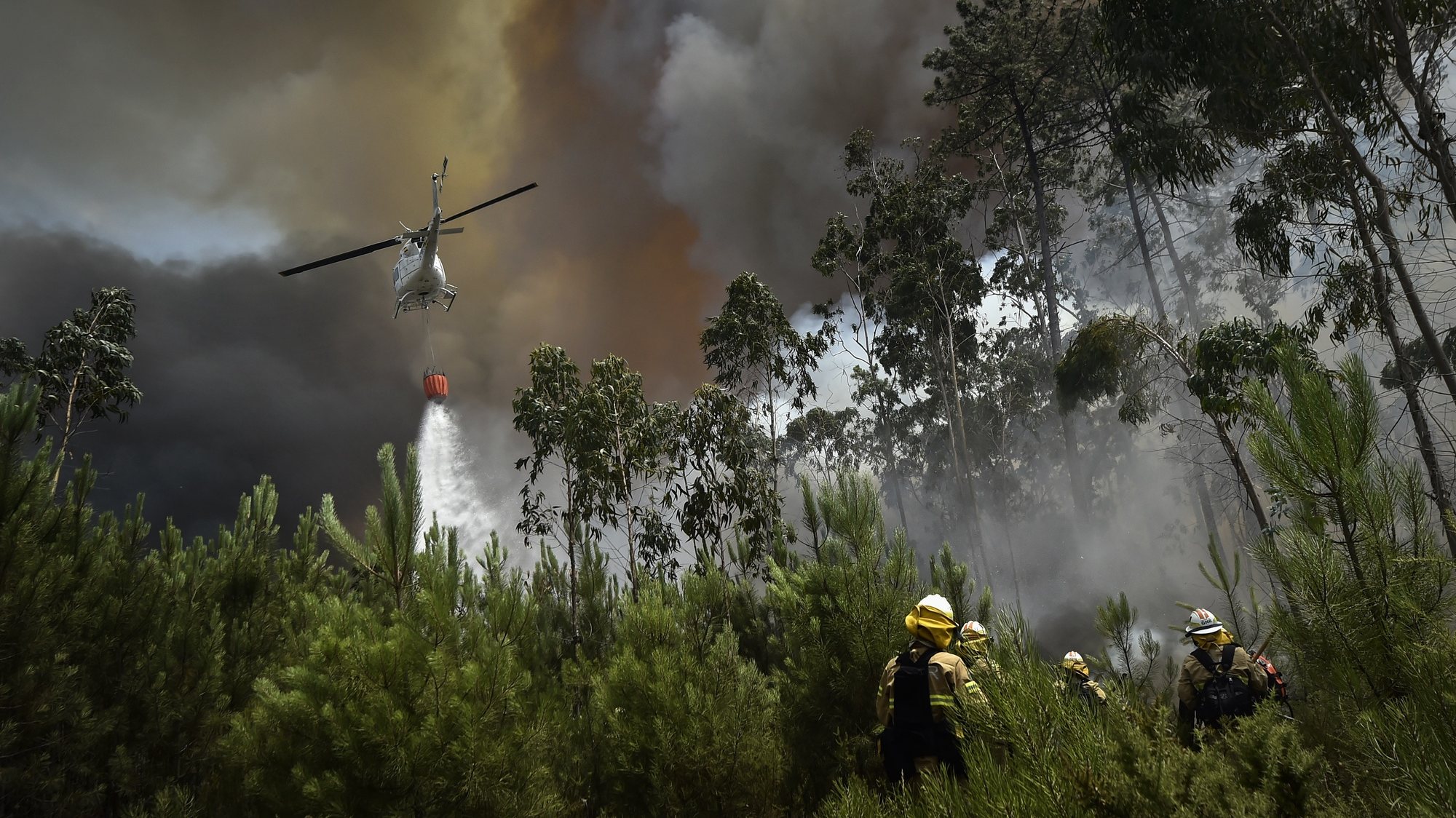 Um helicóptero de combate aos incêndios faz uma descarga de água sobre o fogo perto de elementos da Unidade de Emergência de Proteção e Socorro (UEPS), durante o incêndio florestal na aldeia do Lavradio, Ourém, 13 de julho de 2022. Dezasseis dos 18 distritos de Portugal continental estão hoje sob aviso vermelho, o mais grave, devido ao tempo quente, com mais de uma centena de concelhos em perigo máximo de incêndio rural. NUNO ANDRÉ FERREIRA/LUSA
