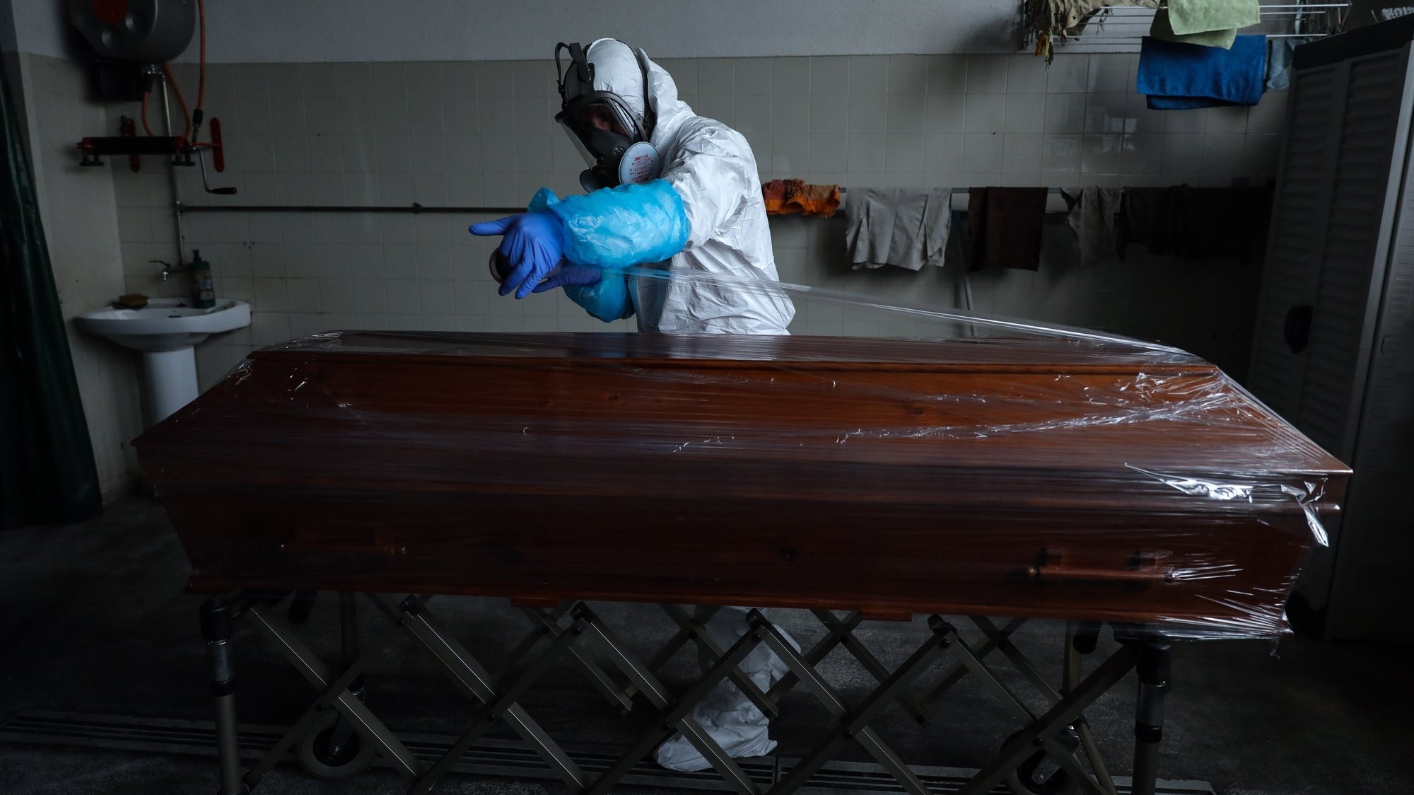 epa08347891 An employee of a funeral home fully protected with an integral mask and wearing protective suits against radioactive contamination and biological agents, covers with plastic wrap the coffin containing a body of a man over 80 years old who died in his home as a victim of covid-19, in Lisbon, Portugal, 03 April 2020 (Issued 07 April 2020). Portugal is in state of emergency until 17 April 2020. Countries around the world are taking increased measures to stem the widespread of the SARS-CoV-2 coronavirus which causes the Covid-19 disease.  EPA/MIGUEL A. LOPES  ATTENTION: This Image is part of a PHOTO SET