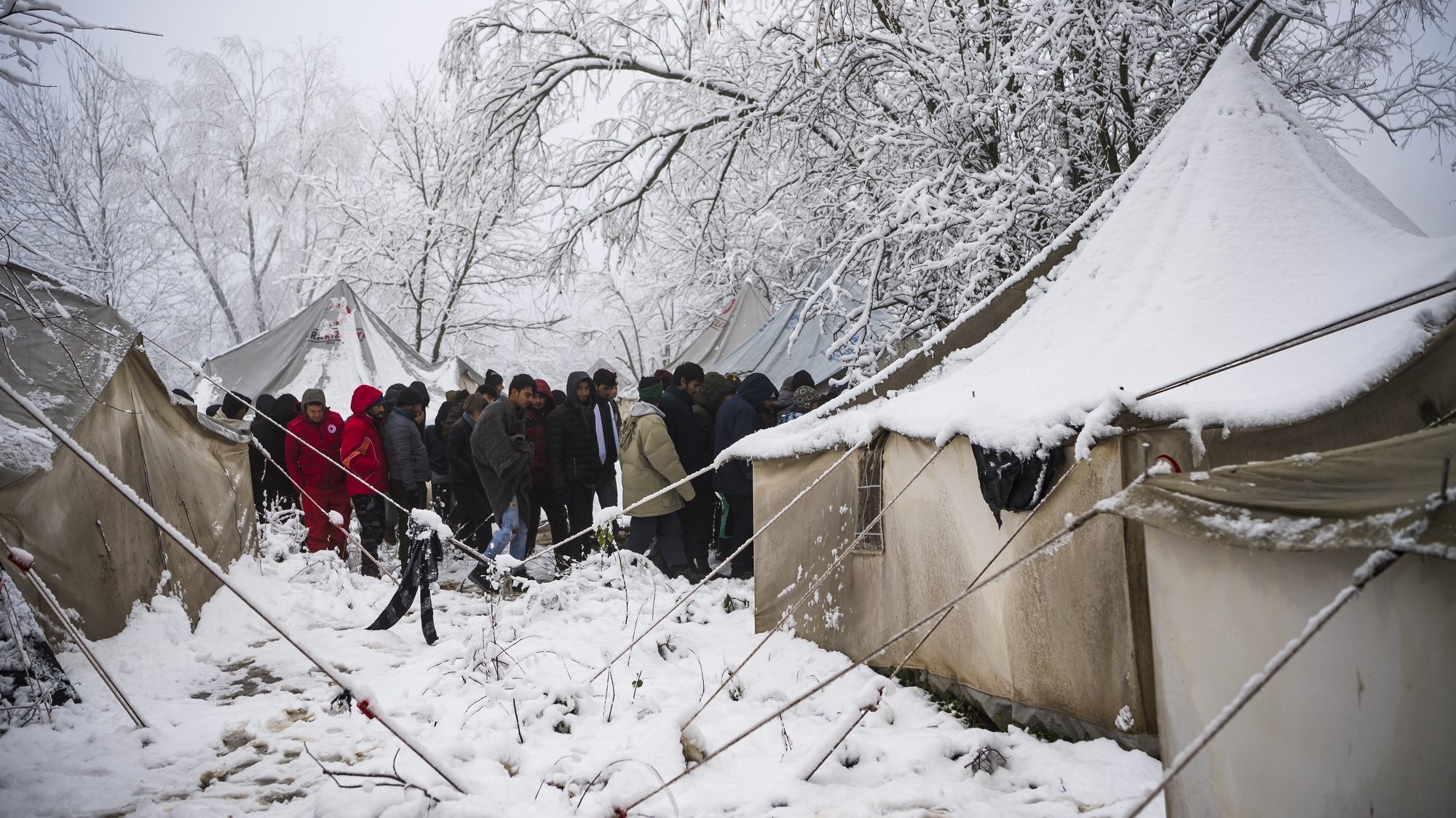 epa08041075 Migrants stand outside from tent during a winter day covered by snow at the Vucjak refugee camp outside Bihac, northwestern Bosnia and Herzegovina, 03 December 2019. According to local media, hundreds of people remain at the camp even after International officials called for it to be shut down.  EPA/JEAN-CHRISTOPHE BOTT