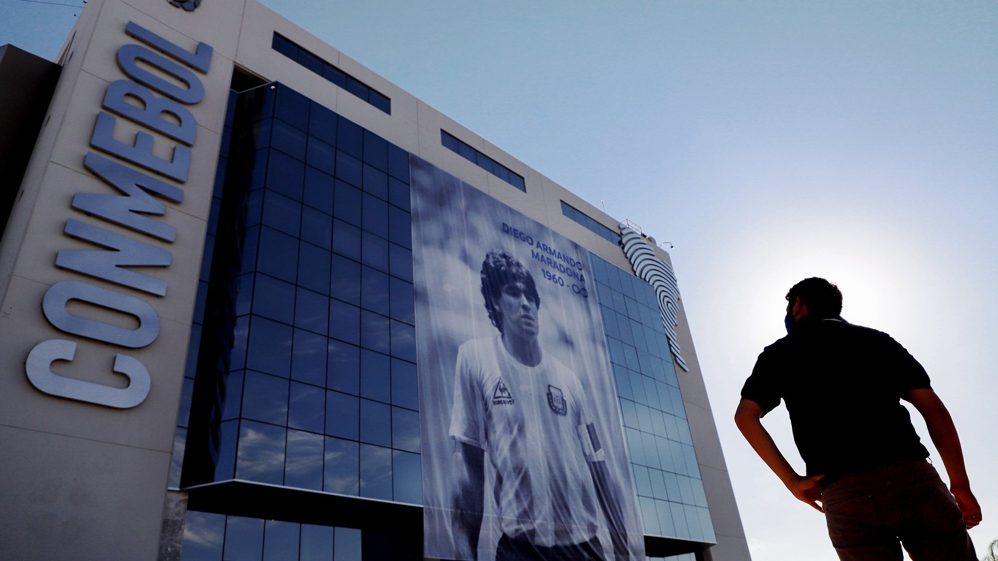 epaselect epa08847393 A man observes a giant banner with a photograph of former Argentine soccer player Diego Armando Maradona, as a tribute, on the facade of the South American Football Confederation (CONMEBOL) building, in Luque, Paraguay, 27 November 2020.  EPA/Nathalia Aguilar