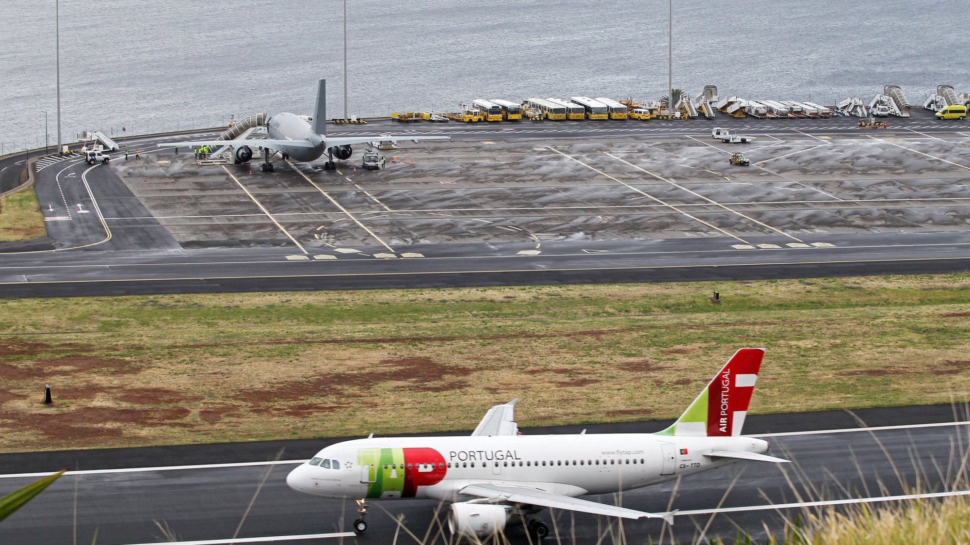 epa07517096 A TAP Airbus A319 airplane (bottom) takes off as persons injured in the 17 April bus crash are boarded onto a German air force airplane (top) to to be flown to Germany, from the airport oif Funchal, Madeira island, Portugal, 20 April 2019. At least 29 German tourists were killed after a bus crashed at the site on Madeira island on 17 April 2019.  EPA/HOMEM GOUVEIA