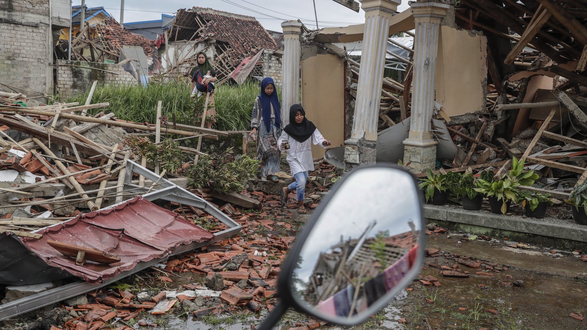 epa10326707 People walk near collapsed houses affected by the 5.6 magnitude earthquake in Cianjur, Indonesia, 25 November 2022. According to the National Disaster Management Authority (BNPB), at least 272 people killed after 5.6 magnitude earthquake hit southwest of Cianjur, West Java on 21 November 2022.  EPA/MAST IRHAM