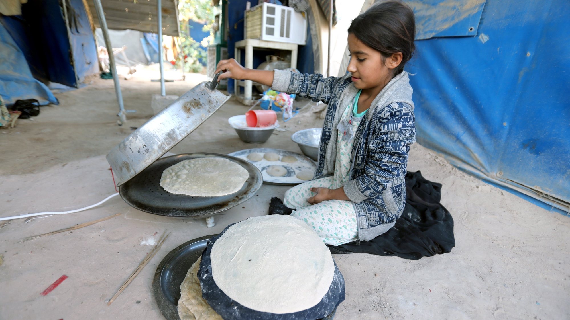 epa10322192 An Iraqi displaced little girl bakes bread at a tent in Amiriyat Al-fallujah camp for refugees, 95 km western Baghdad, Iraq, 23 November 2022.  Al-Amiriya camp hosts about one thousand Sunni families who were forced to flee from their areas in outskirts of Baghdad, Babil, Anbar provinces after the Iraqi security forces backed by Shiite Popular Mobilization groups liberated their areas from the control of the Islamic State group (IS) in October 2014. The displaced said that they are still stuck in the camp after they were unable to return to their homes, despite the end of the battles against ISIS since 2017, but the Ministry of Displacement and Migration had announced that the new Iraqi government was determined to return all the displaced to their homes and to close all the camps for the displaced.  EPA/AHMED JALIL