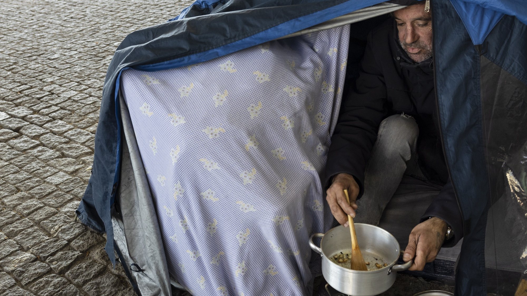 Hermínio Guedes, 46 anos, prepara uma refeição na tenda onde vive no bairro das Fontainhas, no Porto, 31 de janeiro de 2023. Quando na cidade do Porto se junta doenças, falta de habitação, temperaturas quase negativas e enxurradas, o resultado é uma espécie de revolução dos sem-abrigo a montar tendas iglu para combater a vaga de frio no Norte de Portugal. (ACOMPANHA TEXTO DA LUSA DO DIA 05 DE FEVEREIRO DE 2023). JOSÉ COELHO/LUSA