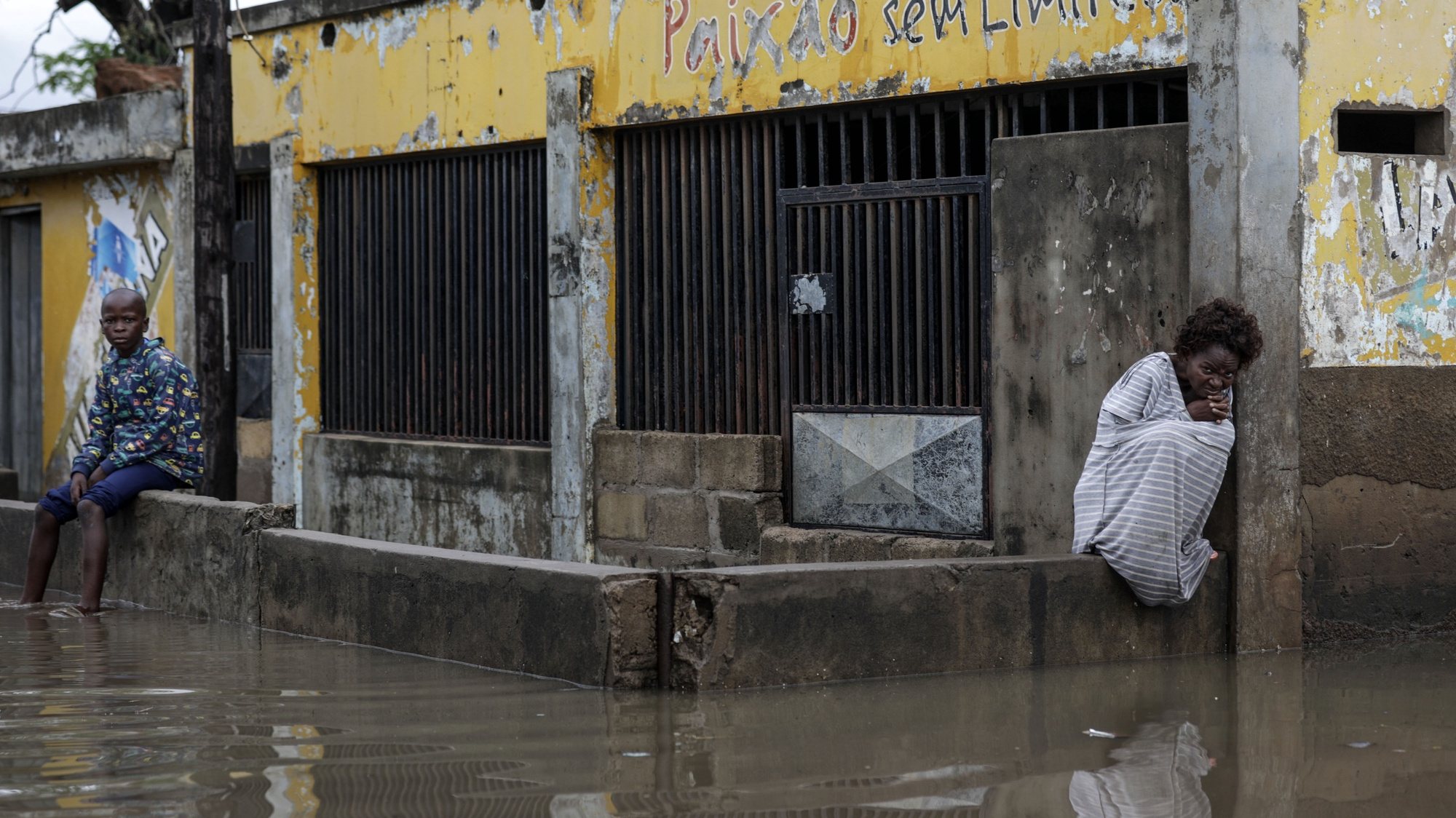 People stand on a wall on a flooded area following rains since 07 of February in Maputo, Mozambique, 09 February 2023. About 2,400 families were left homeless, and dozens of houses flooded in the Mozambican capital. LUISA NHANTUMBO/LUSA
